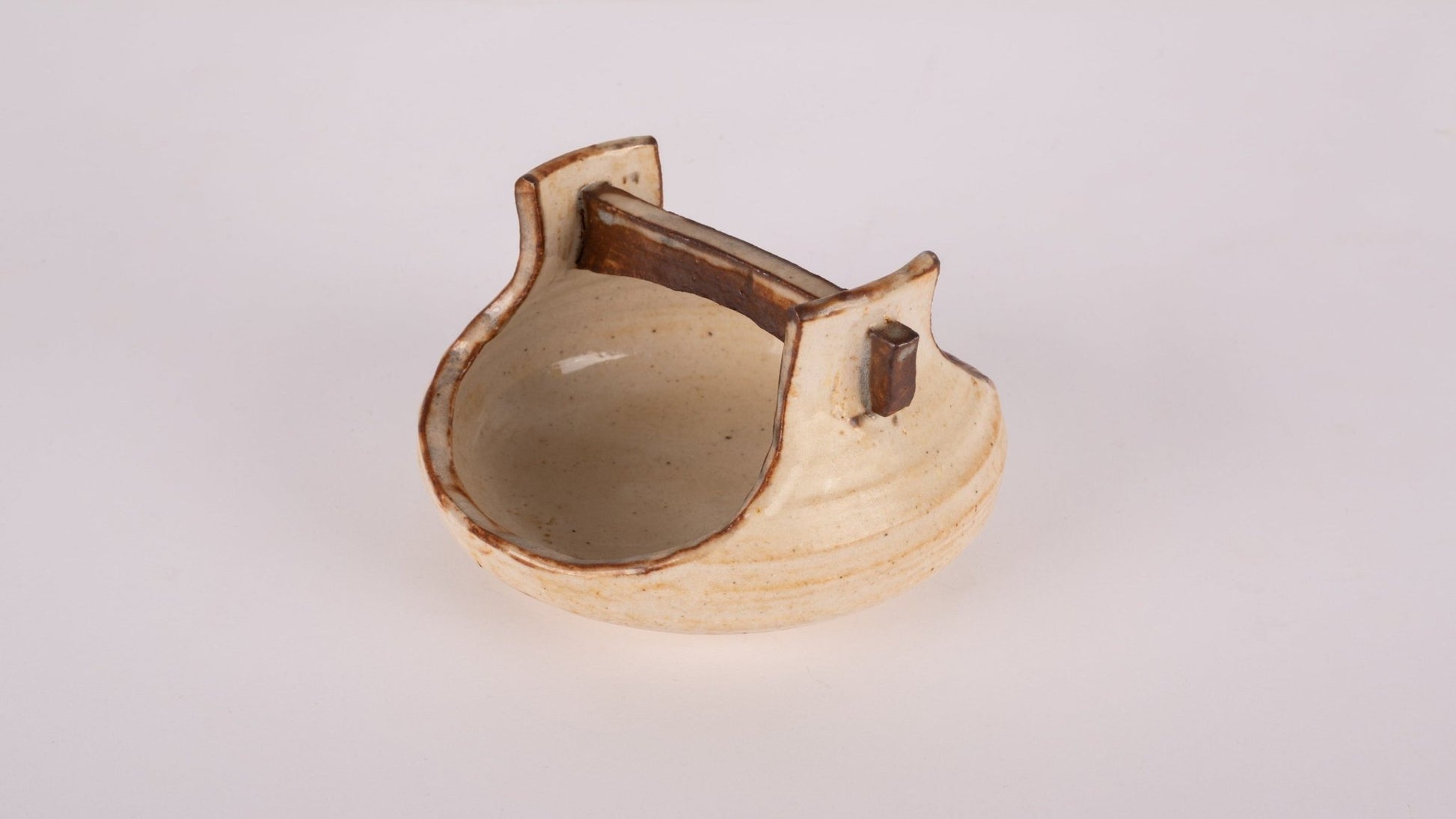 Small studio pottery bowl with handle and stamped signature on bottom, in natural beige glaze finish.