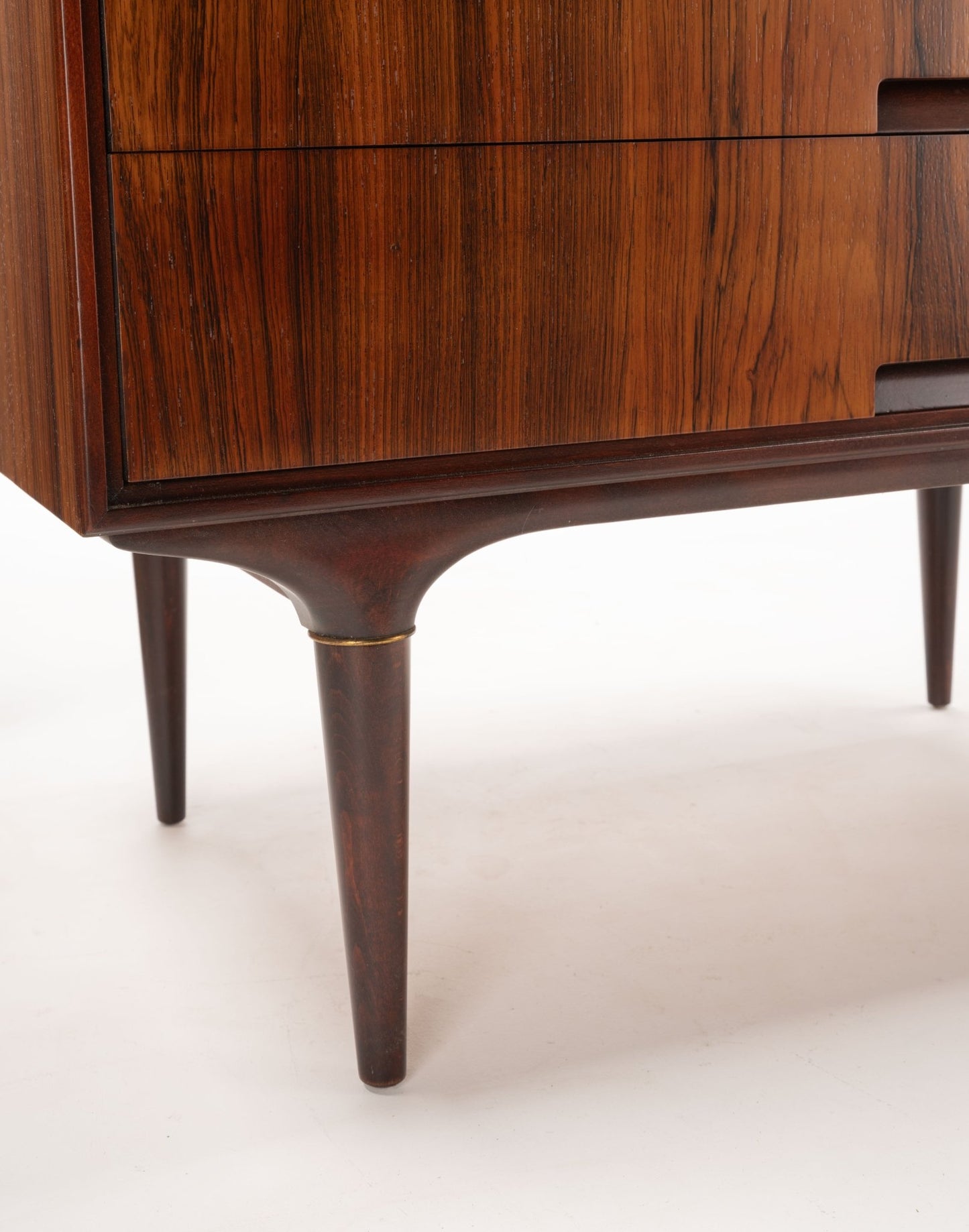 Close-up of mid-century modern rosewood dresser leg with subtle brass accent and bookmatched wood grain panel.