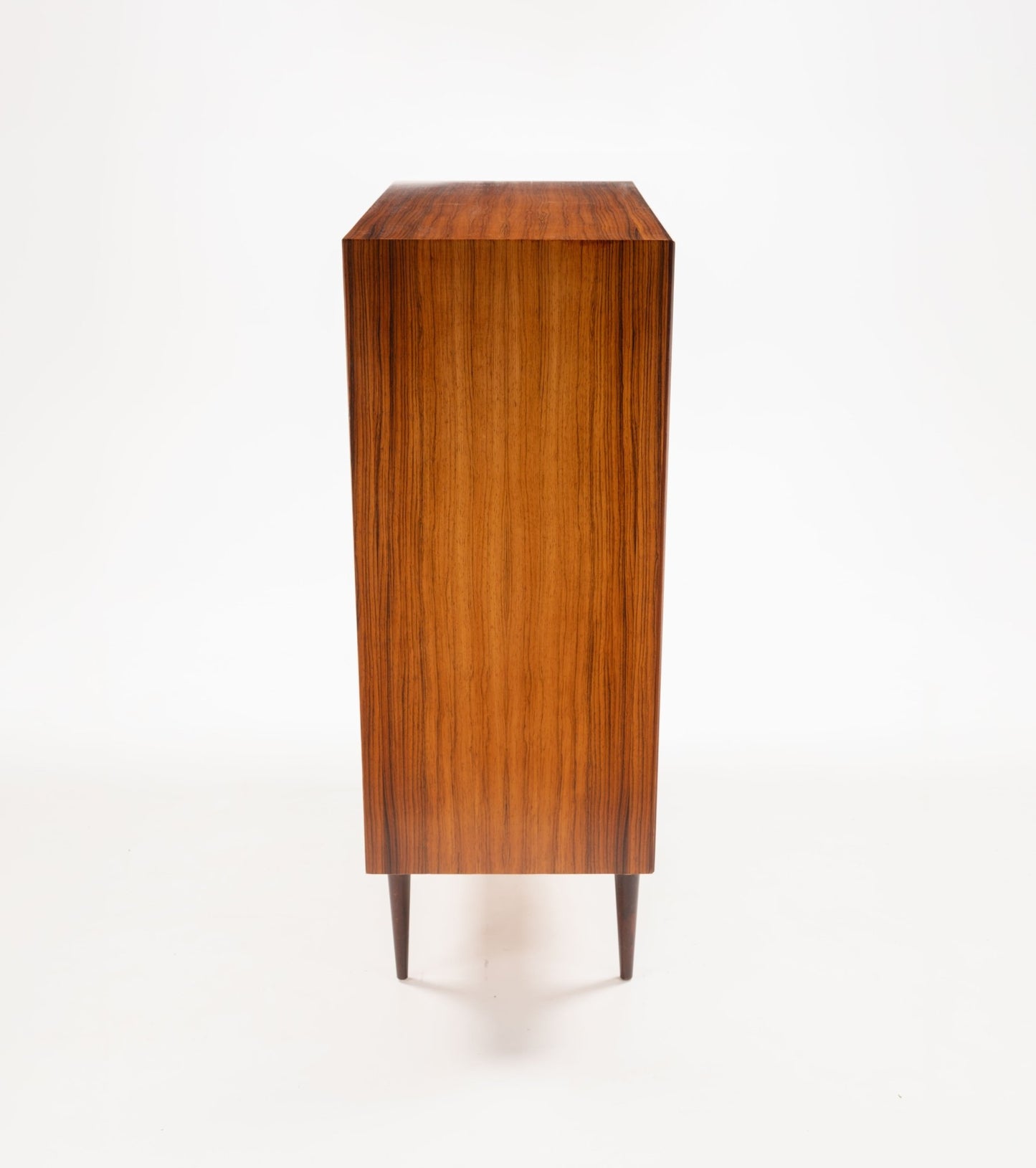 Side view of mid-century modern rosewood dresser with tapered legs and smooth wood grain finish on white background
