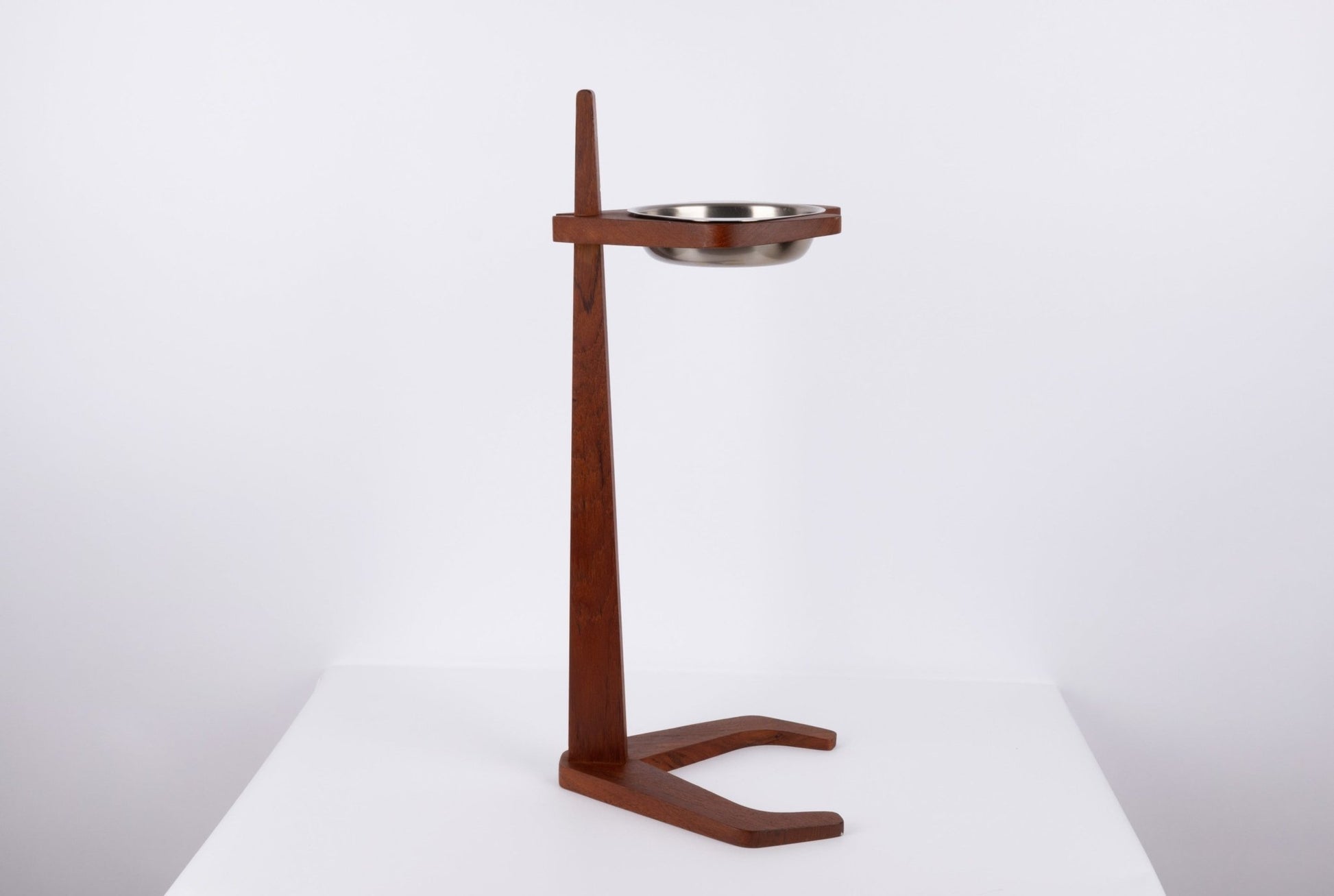 Teak ashtray stand with tapered stem and stylized base holding metal ashtray bowl floating on teak frame