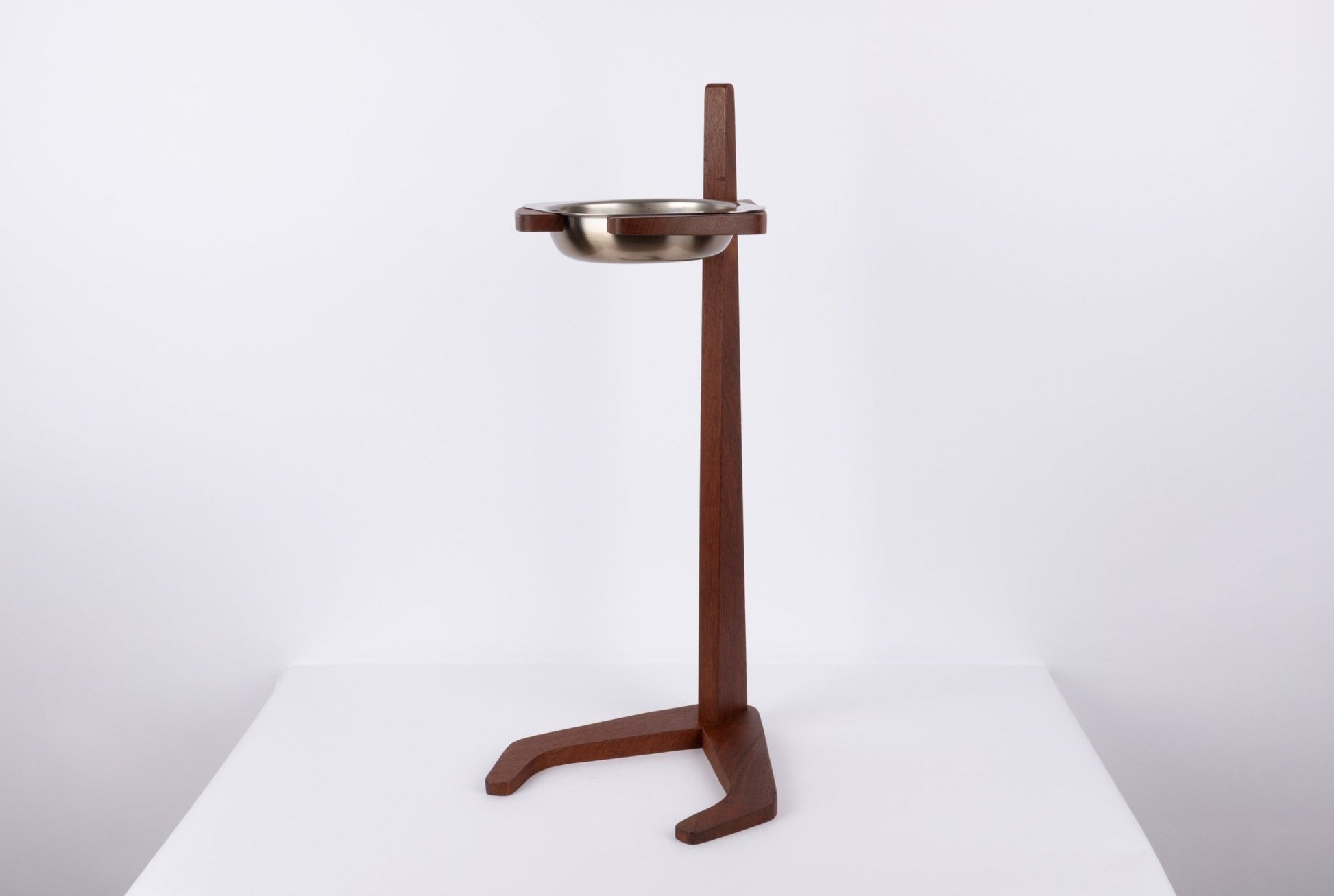 Teak ashtray stand with tapered stem and stylized base holding a floating metal ashtray bowl on a white background.