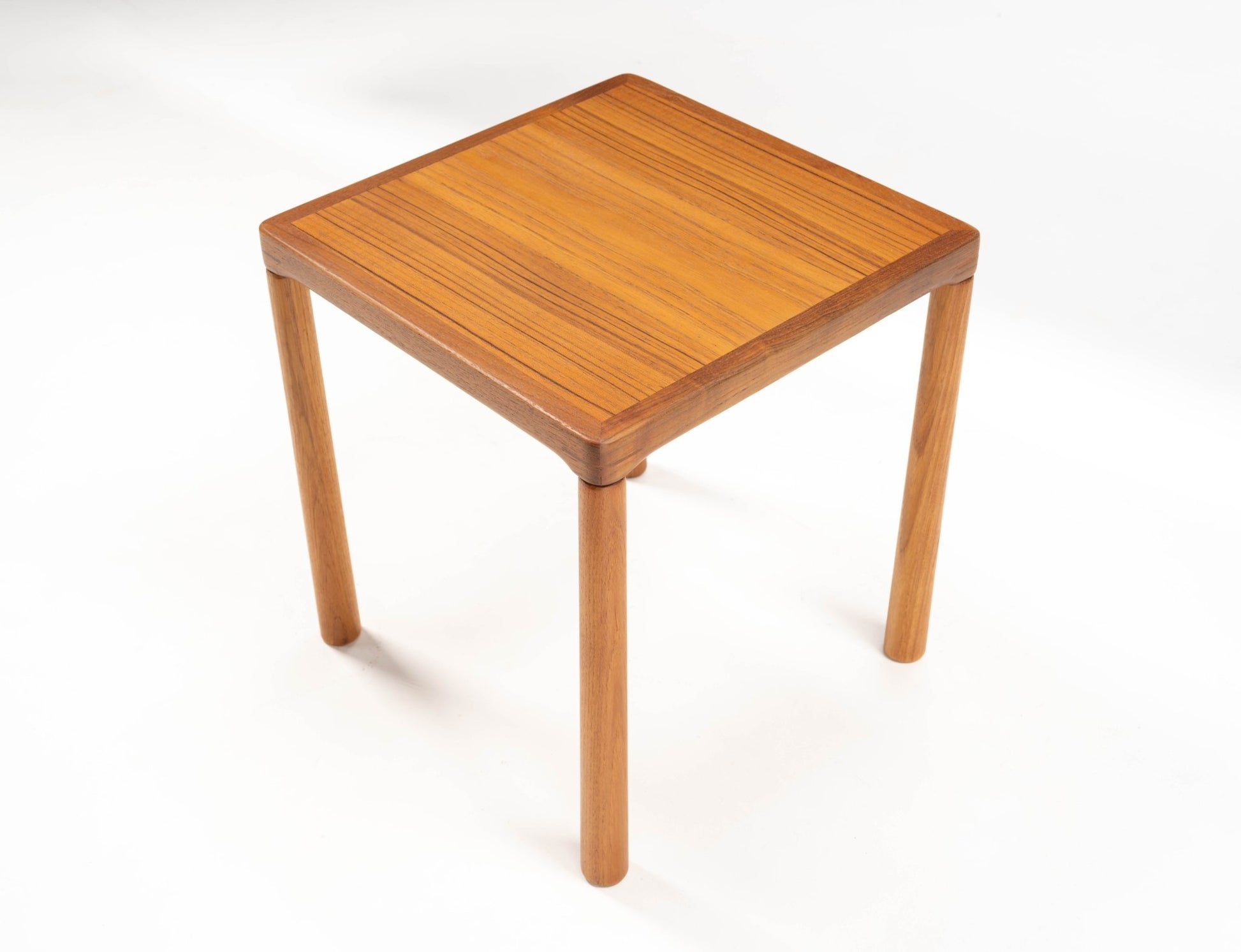 Square mid-century modern teak side table with oak legs and finger joint details on top corners on white background.