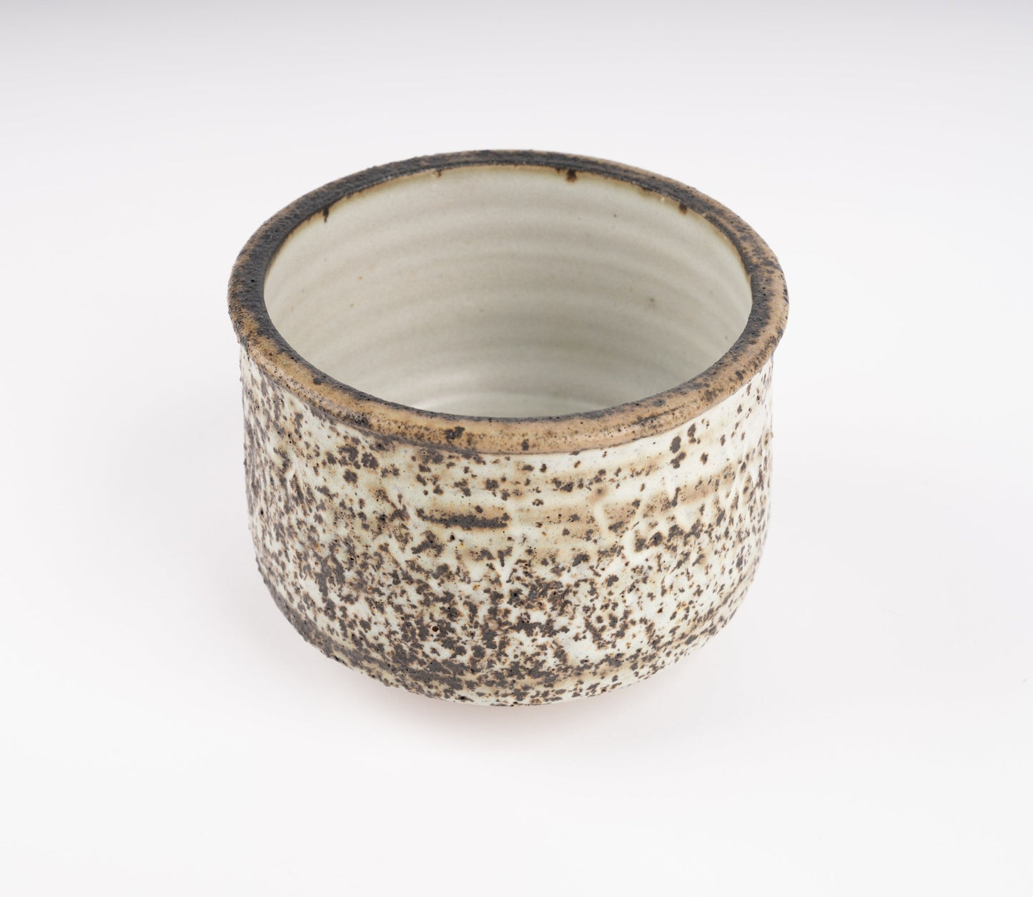 Tessa Kidick studio pottery bowl with low cylindrical form and mottled ivory, charcoal, and earthy brown glaze on raised foot