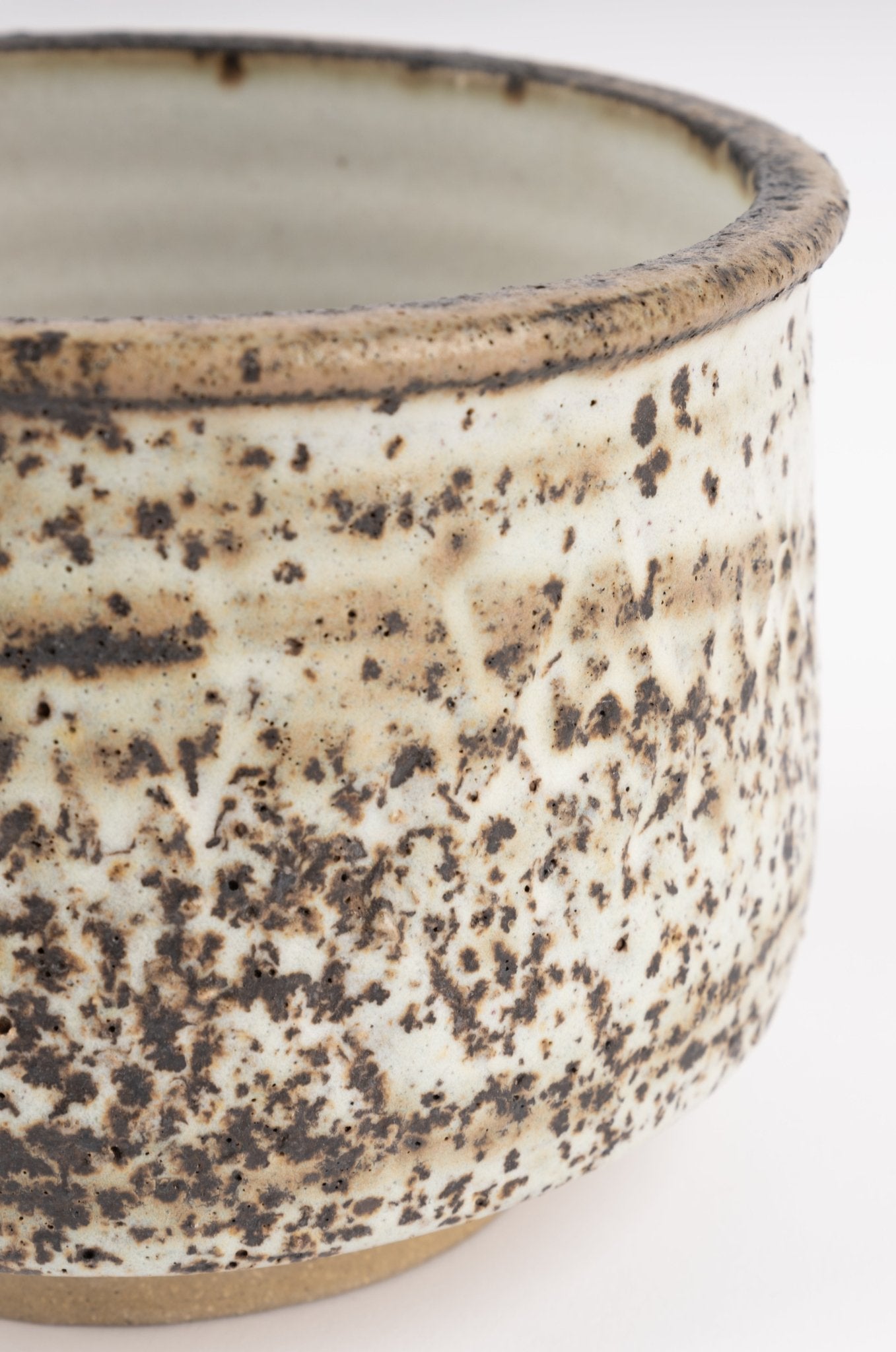 Close-up of Tessa Kidick studio pottery bowl with mottled ivory and brown glazed cylindrical form on raised foot