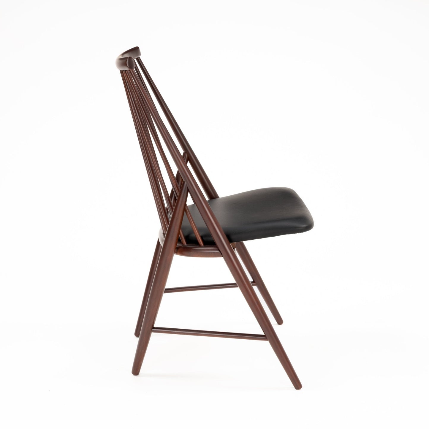 Side profile of dark brown wooden chair with angled spindle backrest and black padded seat cushion