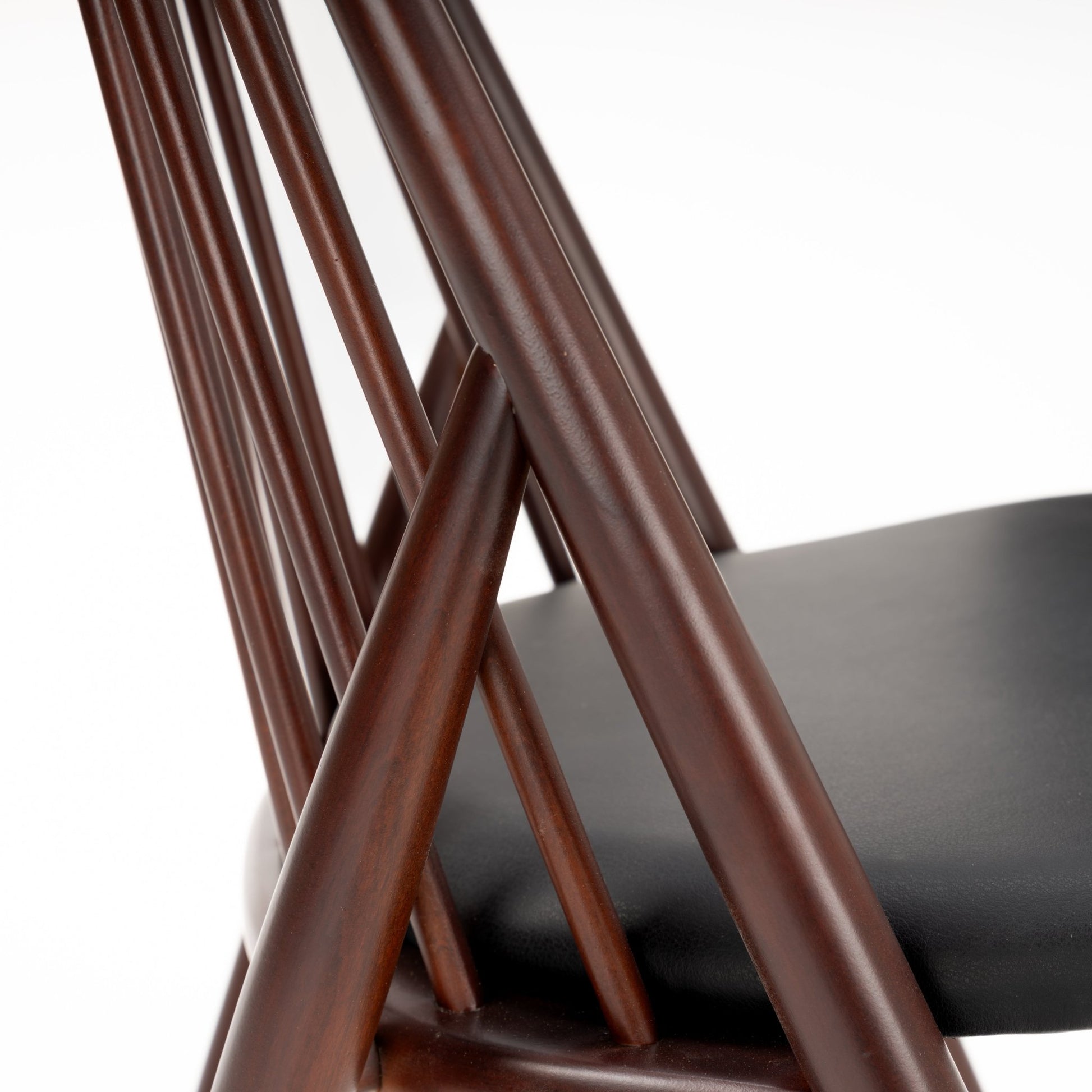 Close-up of dark brown wooden chair with angled spindle backrest and smooth black seat cushion