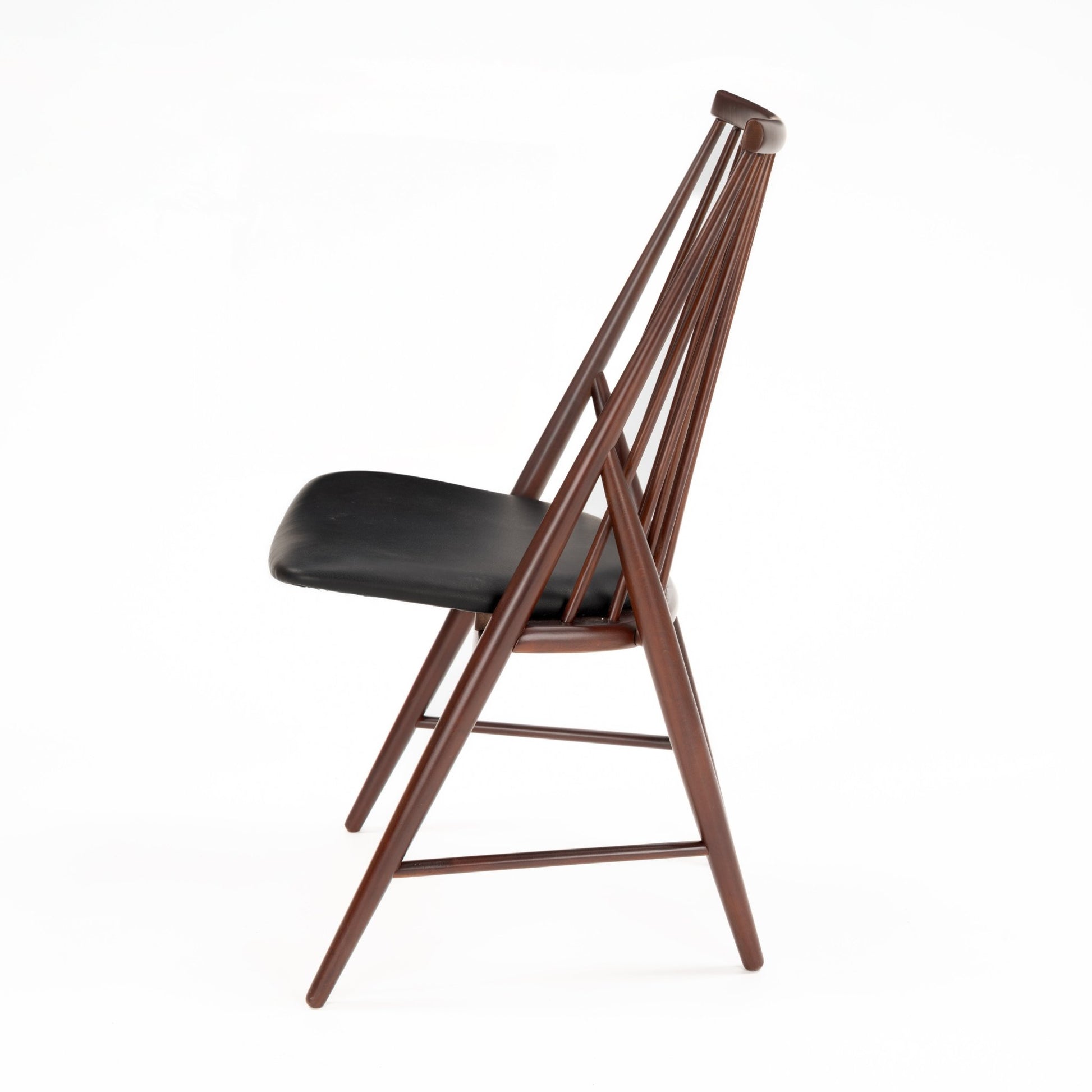 Side profile of wooden chair with angled spindle backrest and black padded seat in dark brown finish