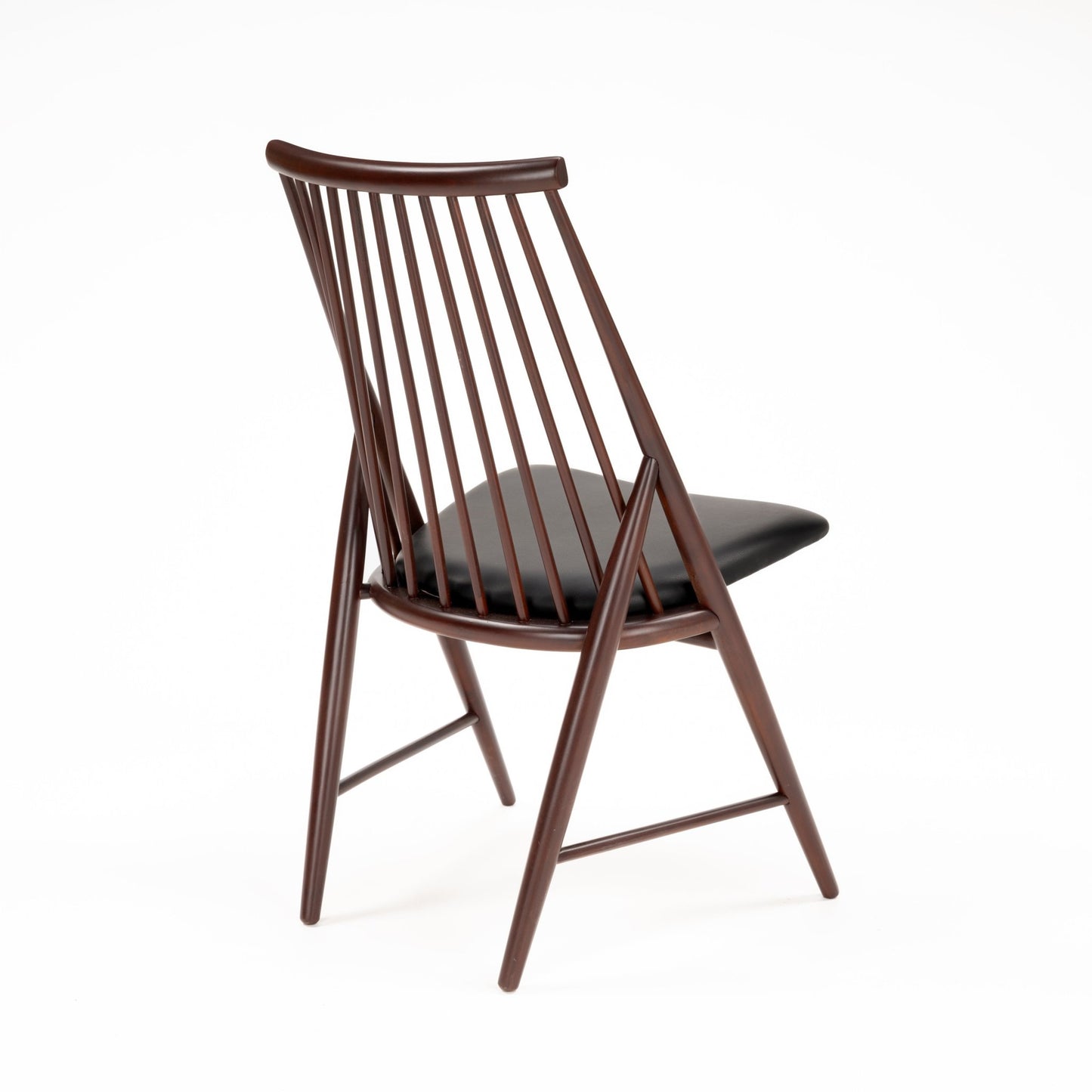 Angled rear view of wooden chair with slender vertical spindles and black leather seat cushion in dark finish