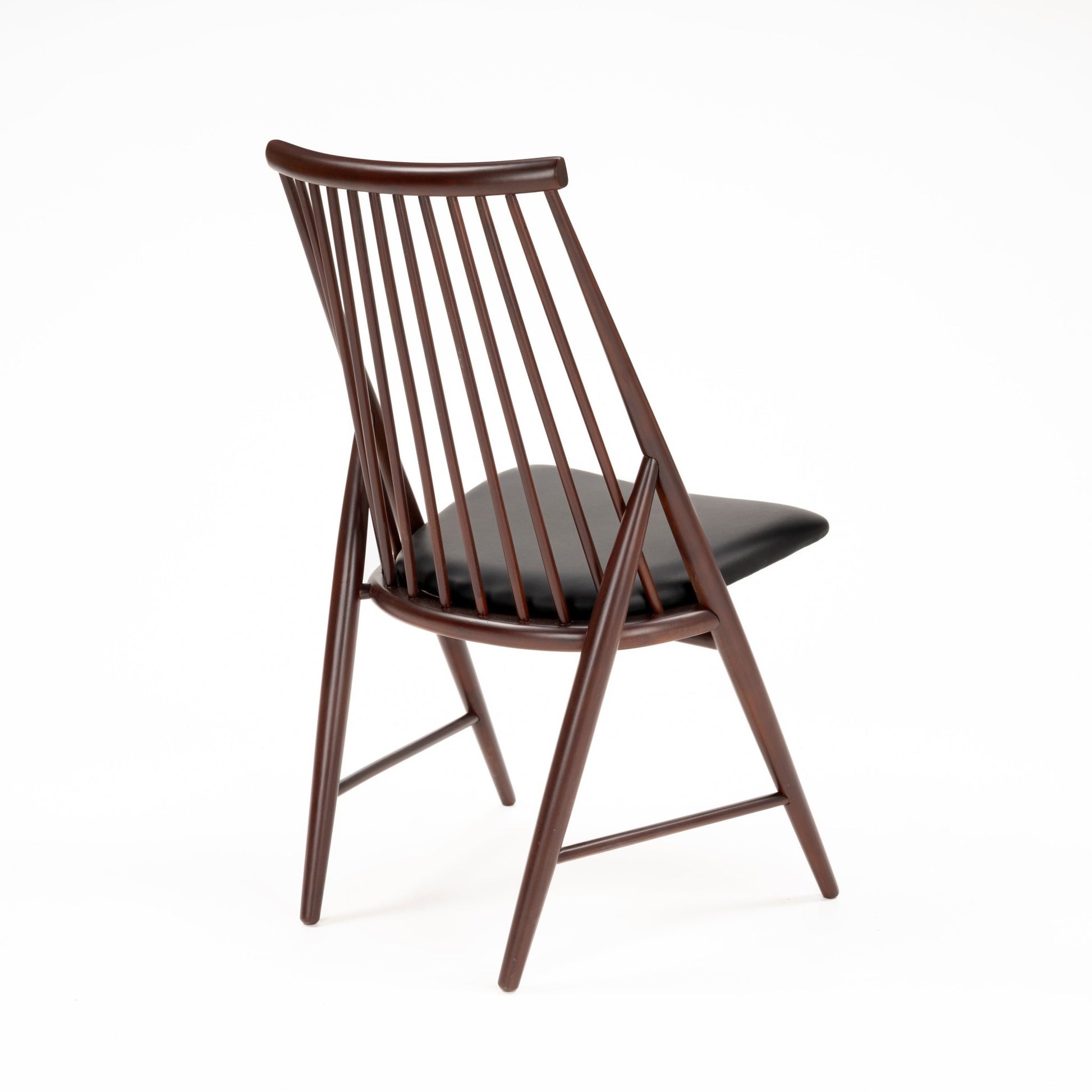 Angled rear view of wooden chair with slender vertical spindles and black leather seat cushion in dark finish