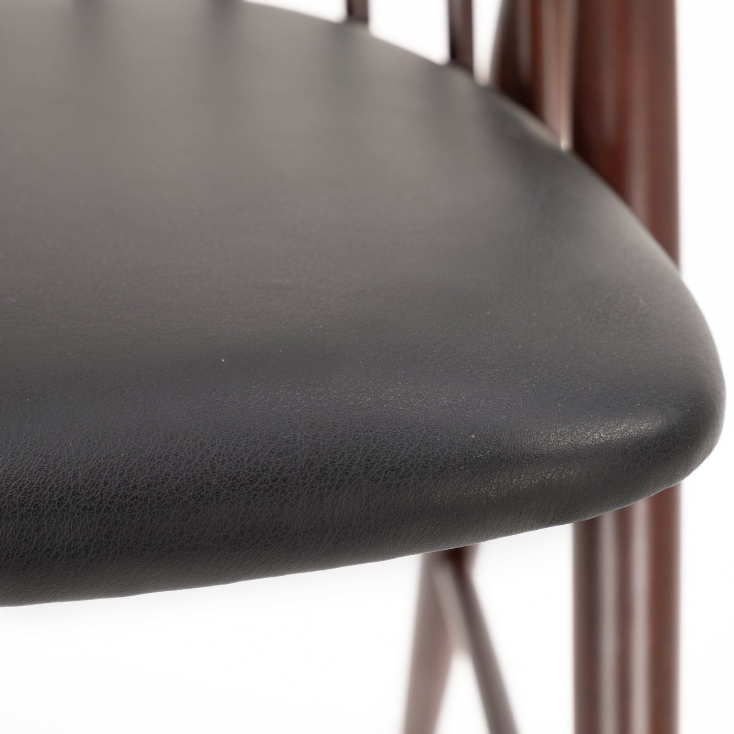 Close-up of smooth black leather seat cushion with rounded edge and dark wooden chair spindles in background