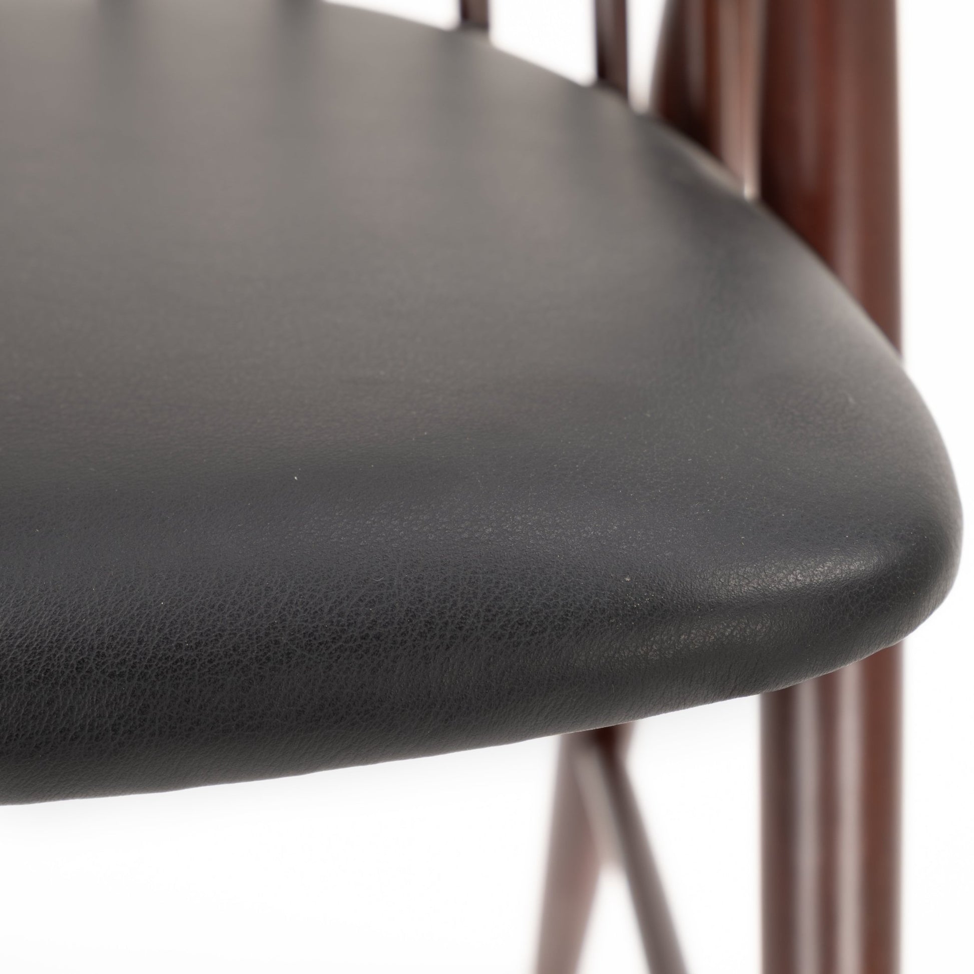 Close-up of smooth black leather seat cushion with rounded edge and dark wooden chair spindles in background