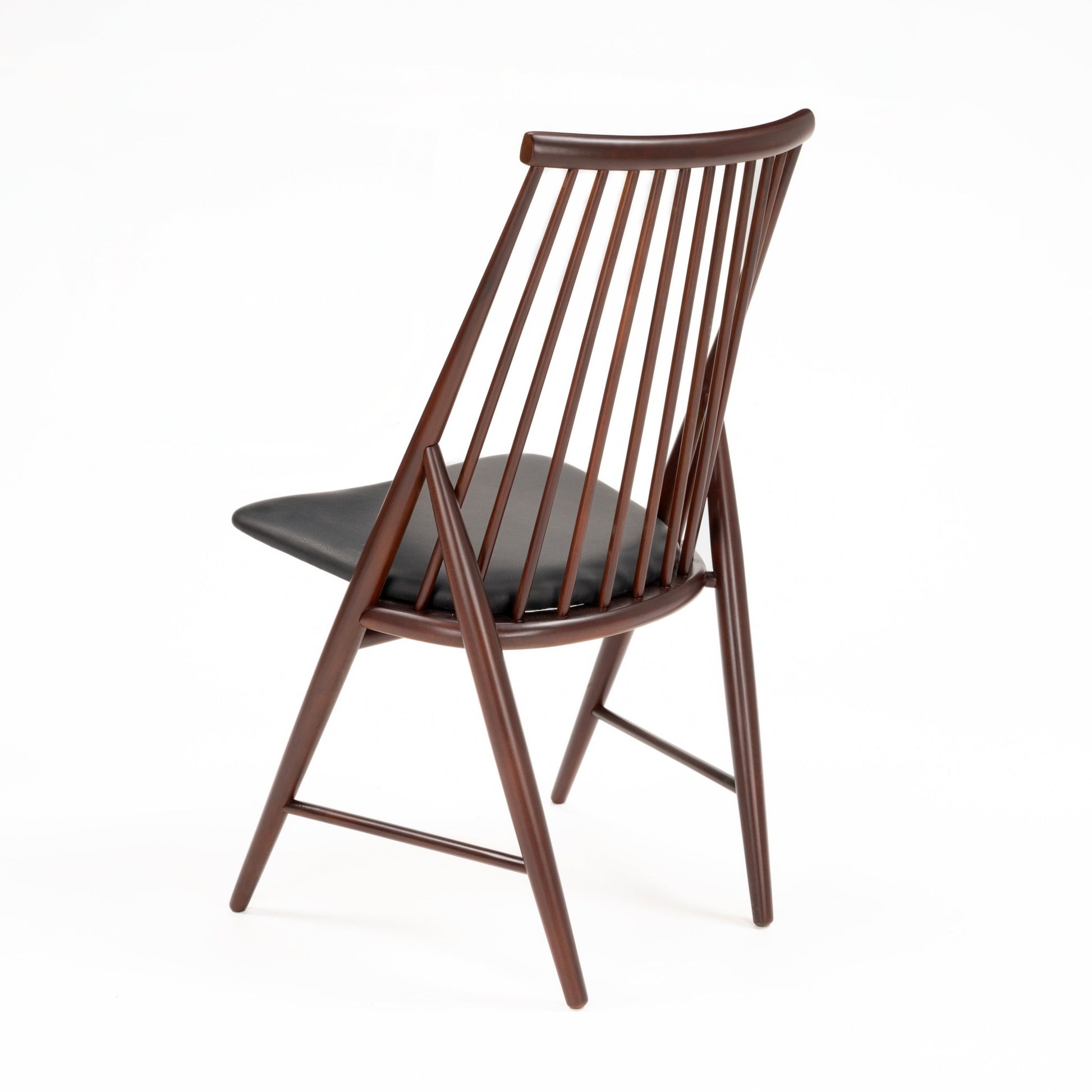 Rear angled view of wooden chair with tall spindle backrest and black padded seat in dark brown finish