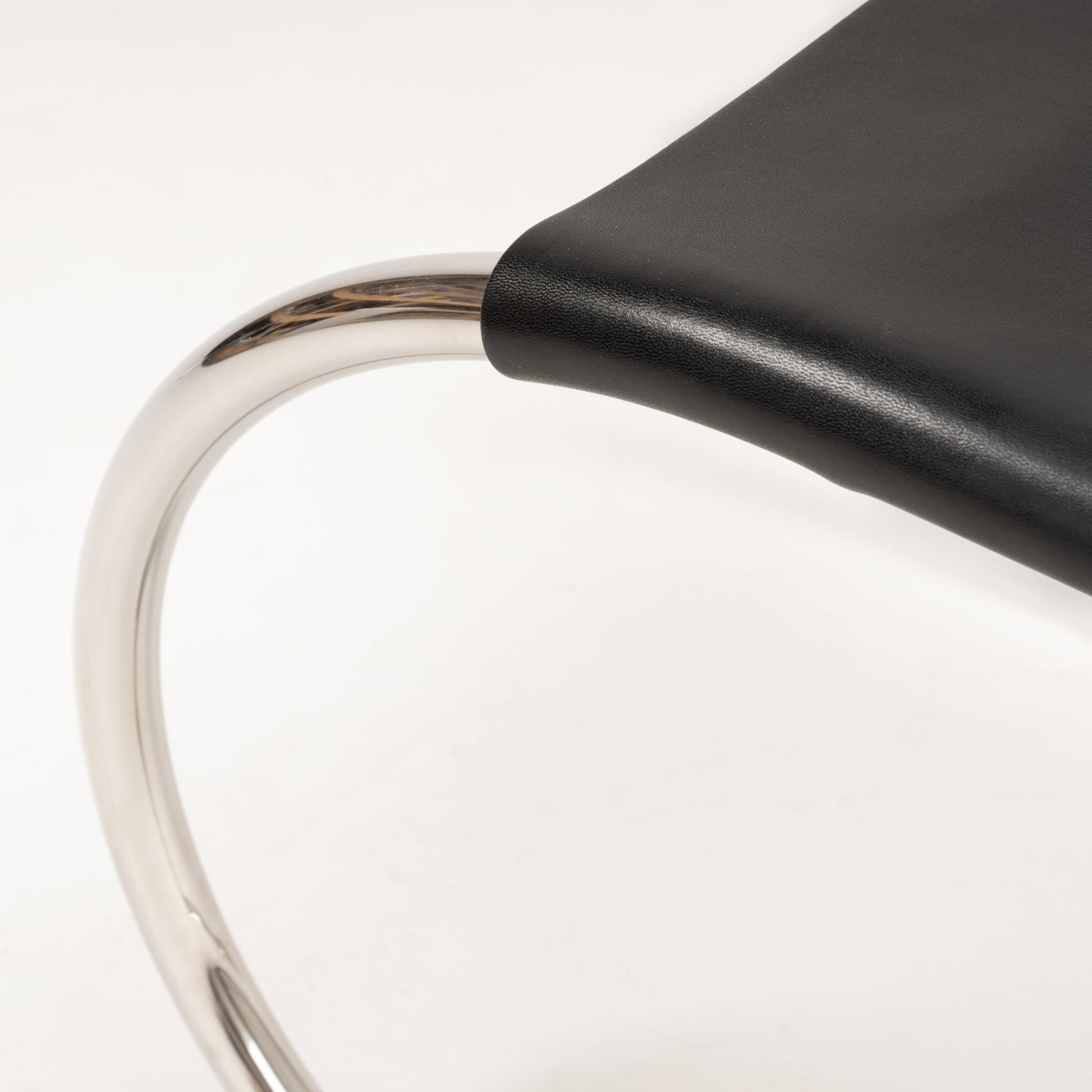 Close-up of polished chrome tubular frame and smooth black leather seat of Van Der Rohe MR10 cantilever chair