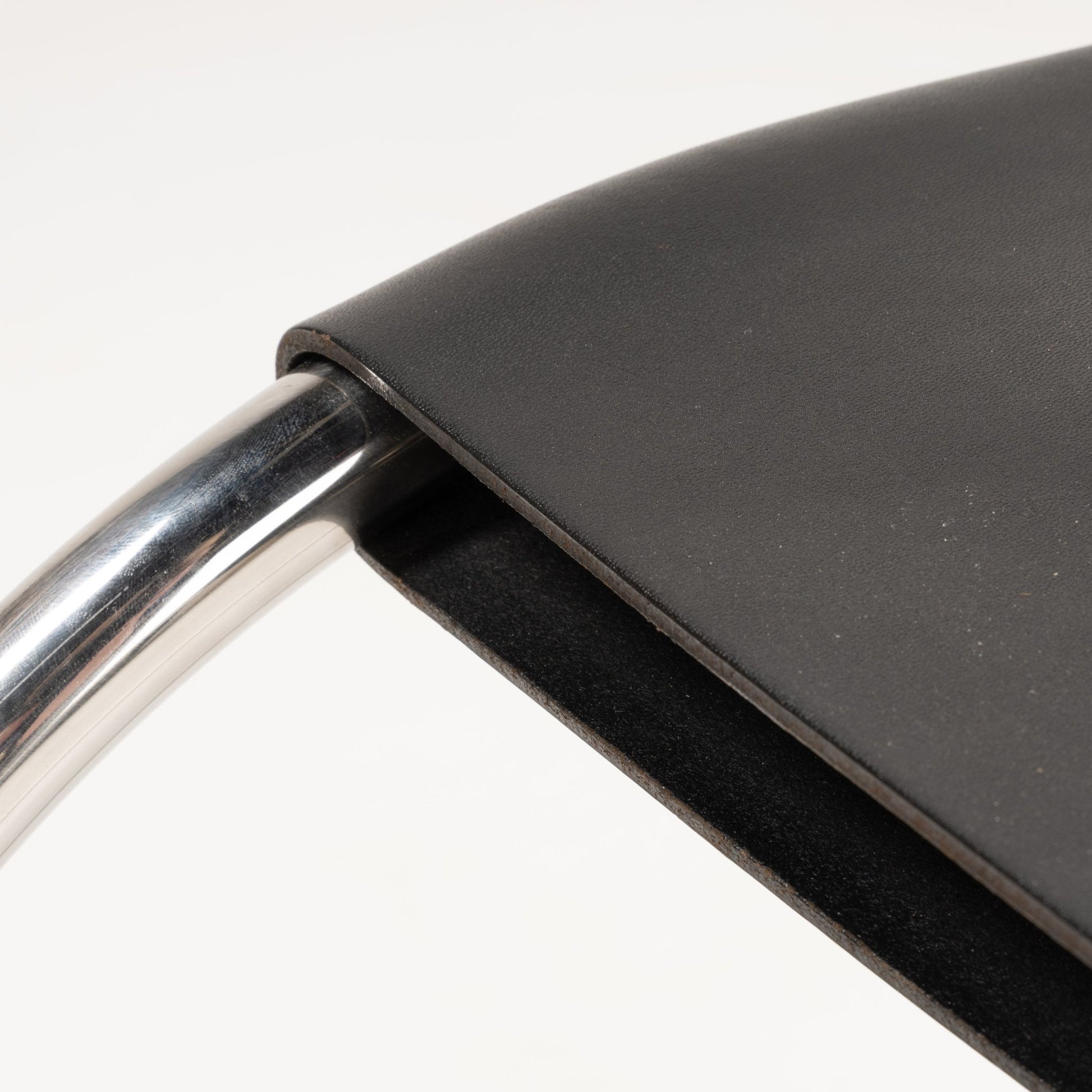 Close-up of polished chrome frame curving beneath smooth black leather seat of Van Der Rohe MR10 cantilever chair