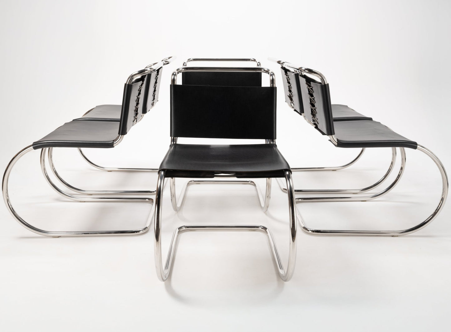 Front view of six Van Der Rohe MR10 cantilever chairs with polished chrome tubular frames and black leather seats and backs