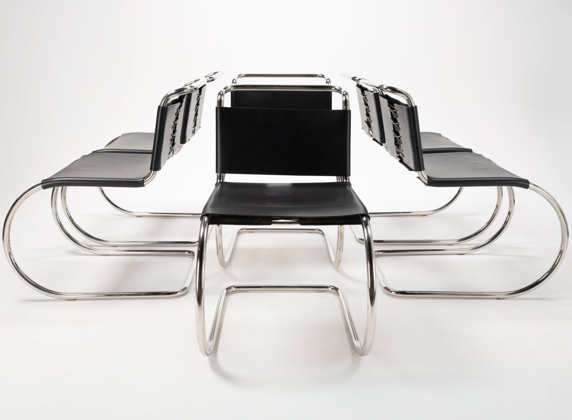 Front view of six Van Der Rohe MR10 cantilever chairs with polished chrome tubular frames and black leather seats and backs