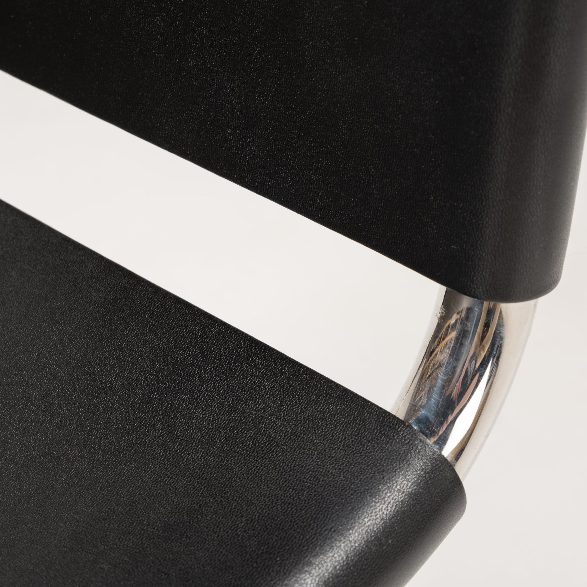 Detailed close-up of polished chrome tubular steel frame connecting smooth black leather seat and backrest on MR10 chair