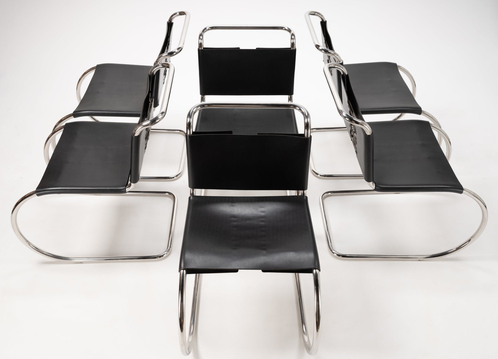 Overhead view of six Van Der Rohe MR10 cantilever chairs with polished chrome frames and black leather seats and backs