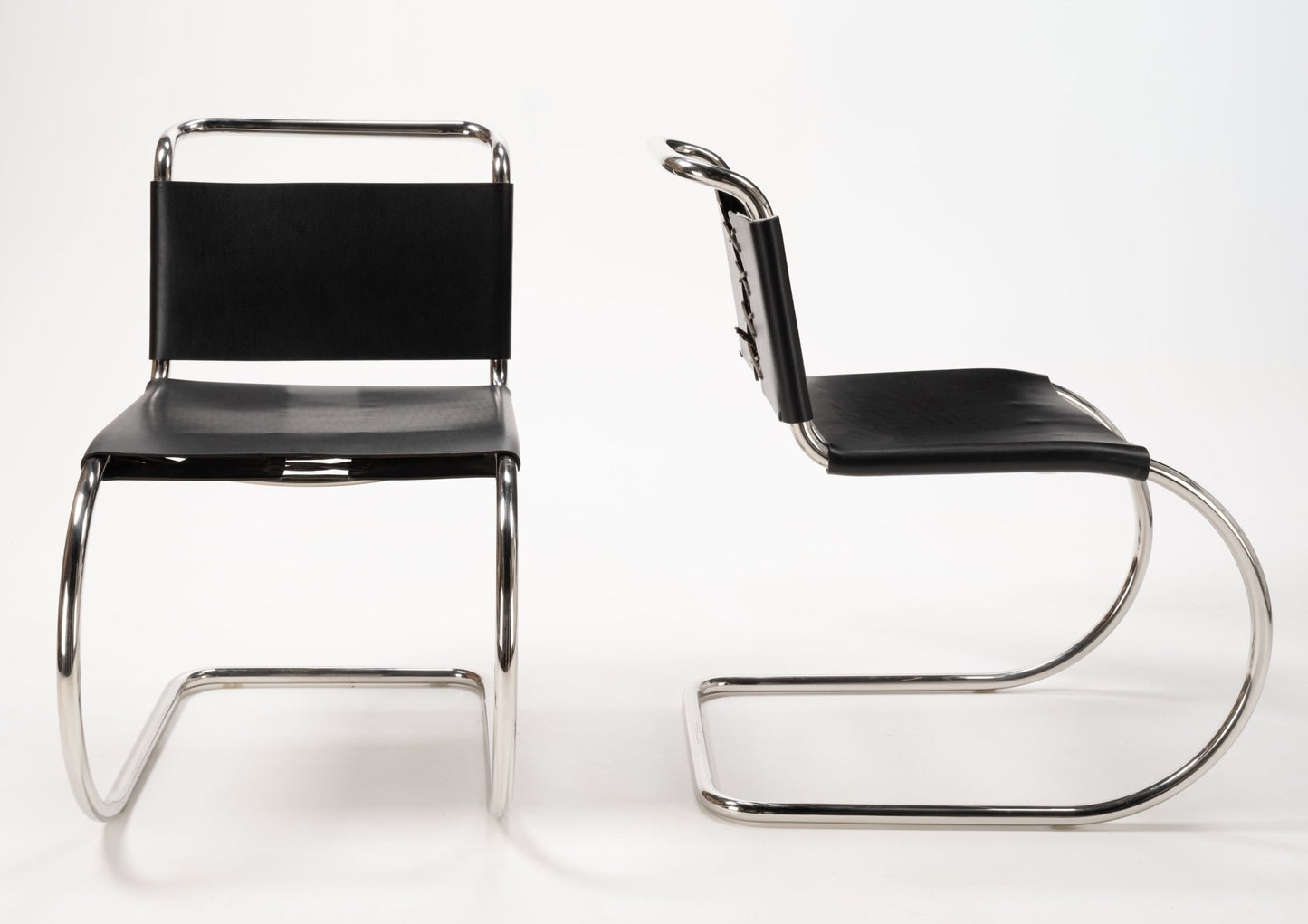 Two Van Der Rohe MR10 cantilever chairs with polished chrome tubular frames and black leather seats and backs