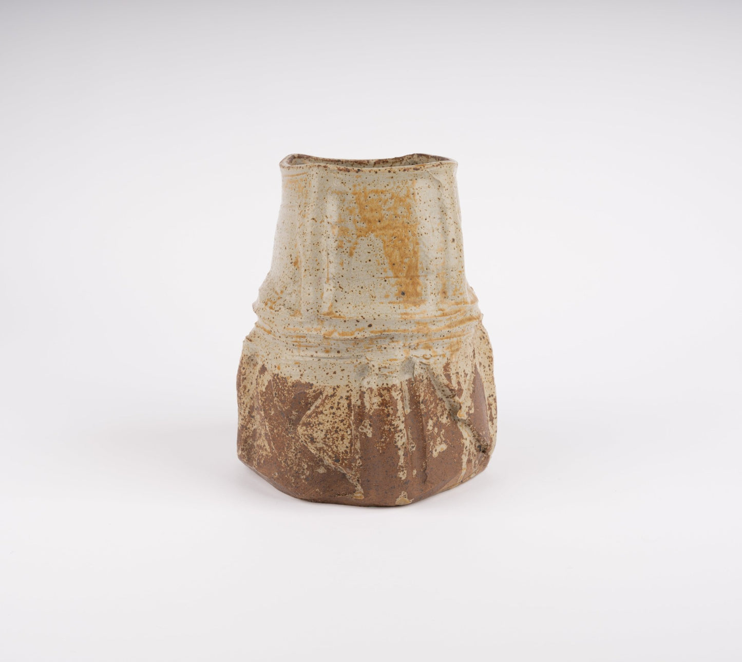 Wabi-Sabi inspired studio pottery vase with organic uneven form and textured beige and brown glaze on white background