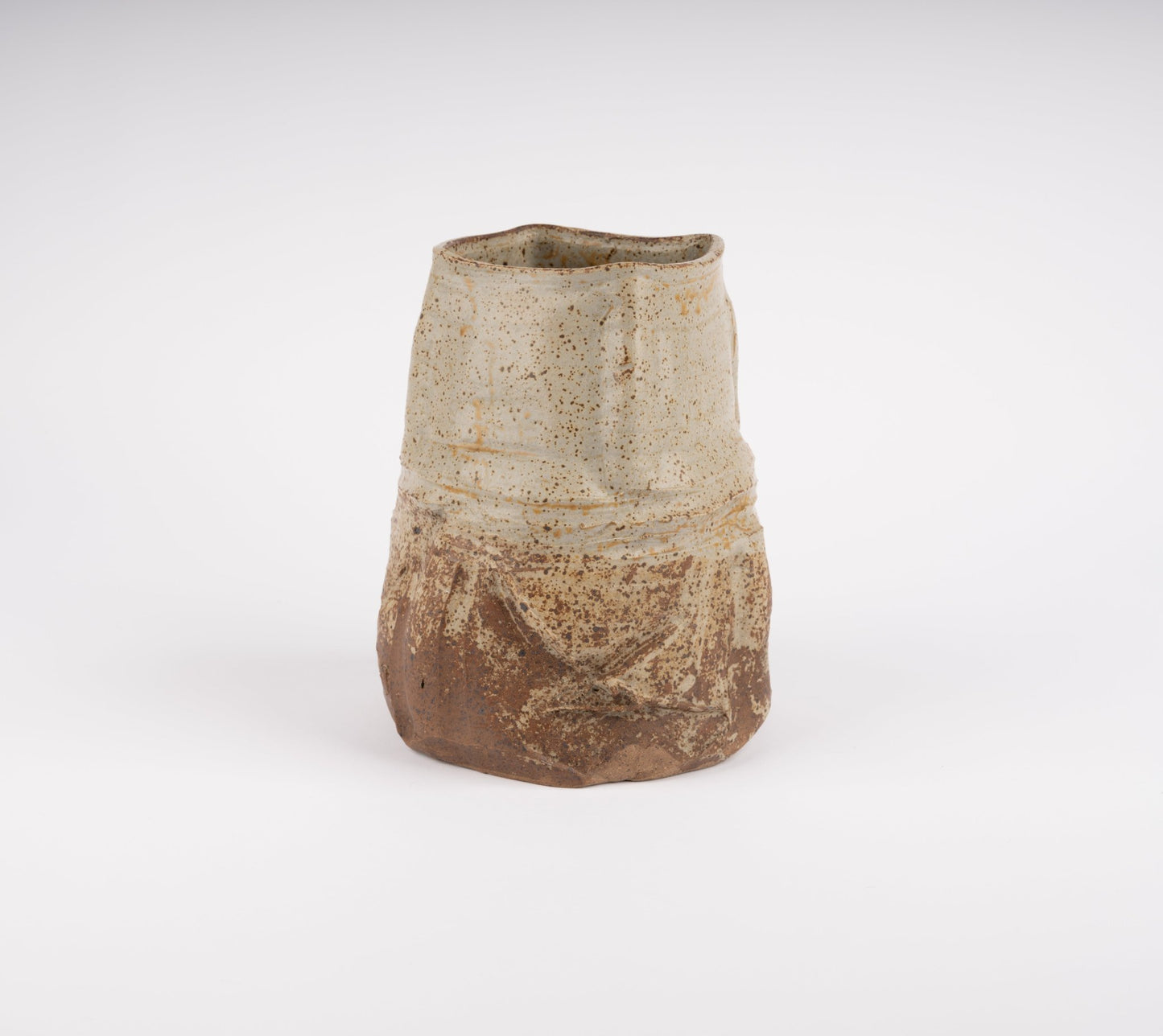 Wabi-Sabi inspired studio pottery vase with irregular silhouette and textured beige and brown glaze on white background