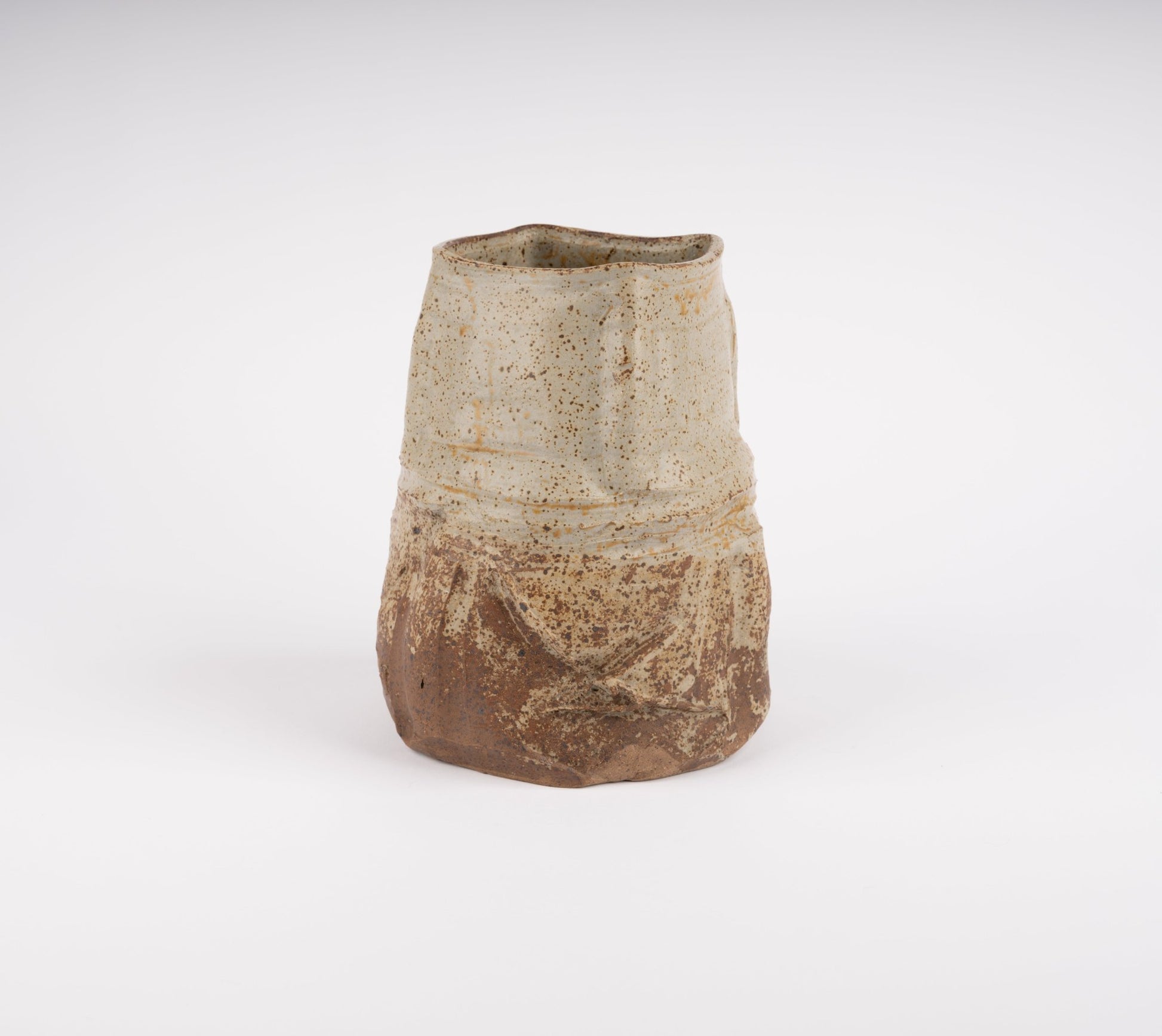 Wabi-Sabi inspired studio pottery vase with irregular silhouette and textured beige and brown glaze on white background