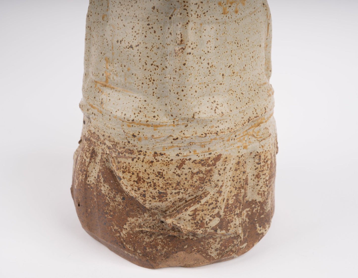 Close-up of wabi-sabi inspired studio pottery vase with speckled beige and brown textured glaze on white background