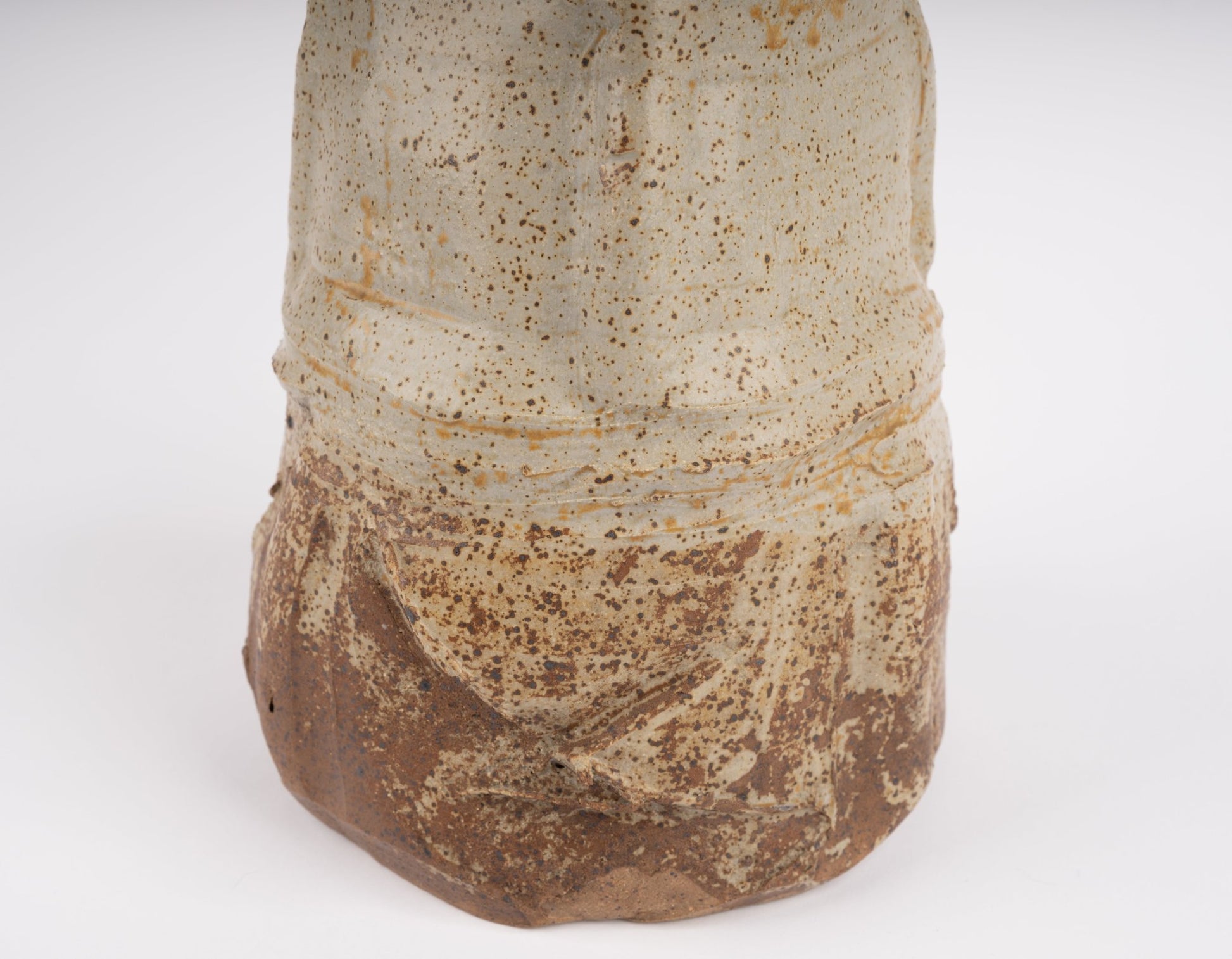 Close-up of wabi-sabi inspired studio pottery vase with speckled beige and brown textured glaze on white background