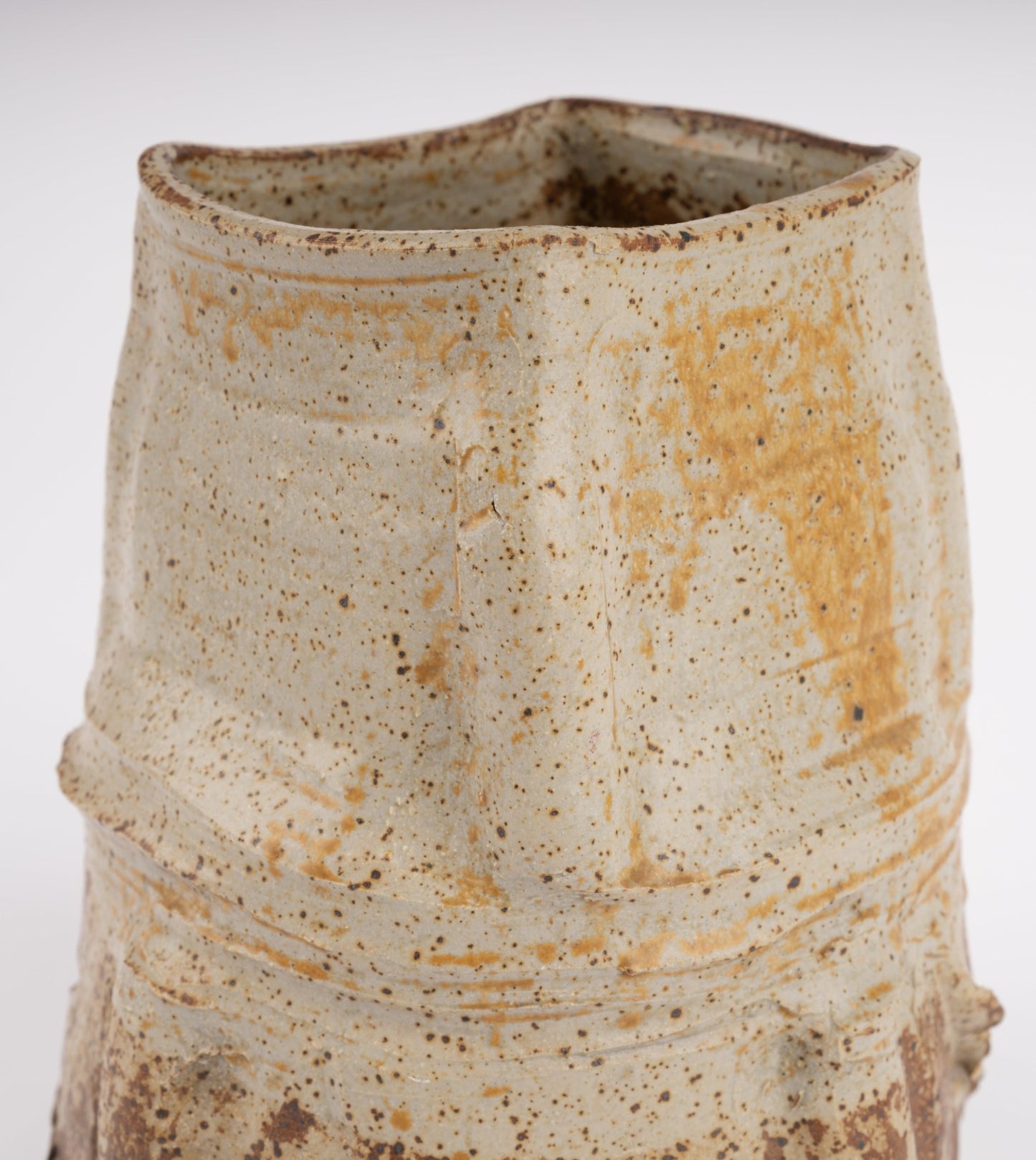 Handcrafted ceramic vase with irregular organic shape and speckled beige glaze in wabi-sabi style on white background