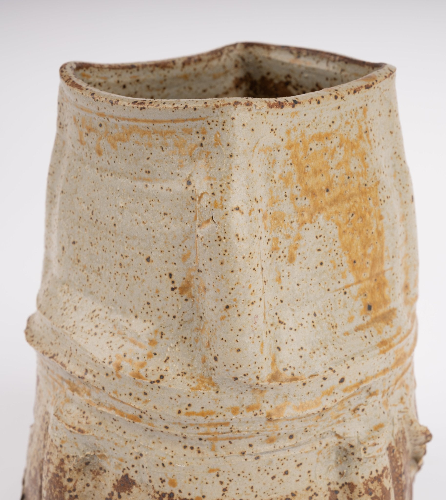 Handcrafted ceramic vase with irregular organic shape and speckled beige glaze in wabi-sabi style on white background