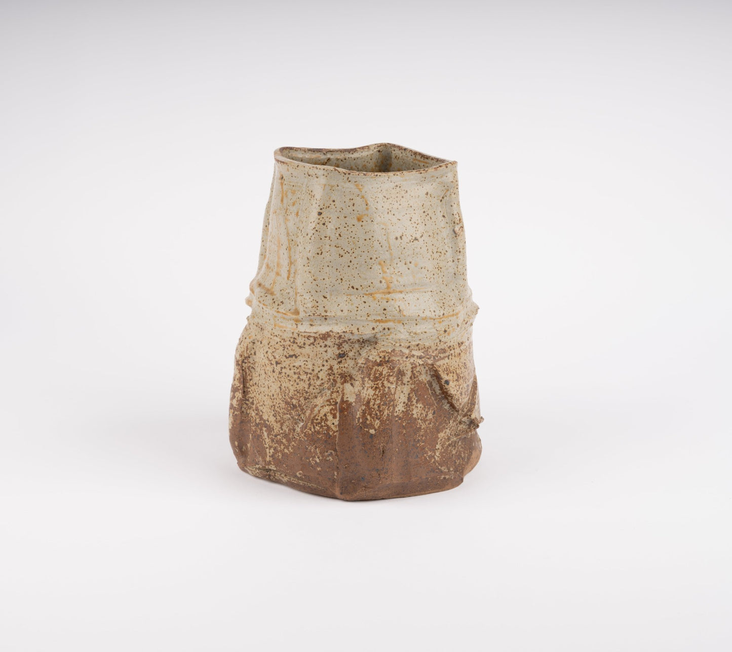 Wabi-Sabi inspired studio pottery vase with irregular form, textured beige and brown glaze on white background