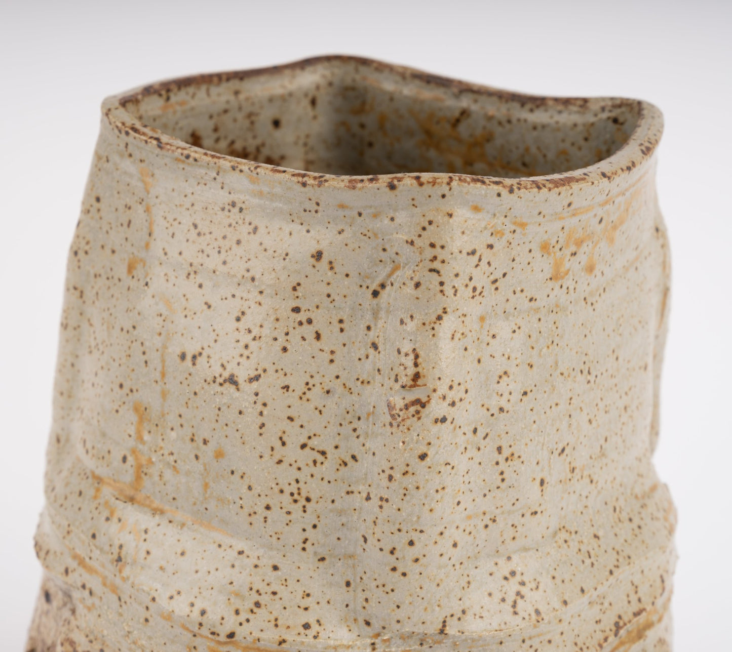 Wabi-Sabi inspired studio pottery vase with irregular organic form and speckled beige textured glaze on white background
