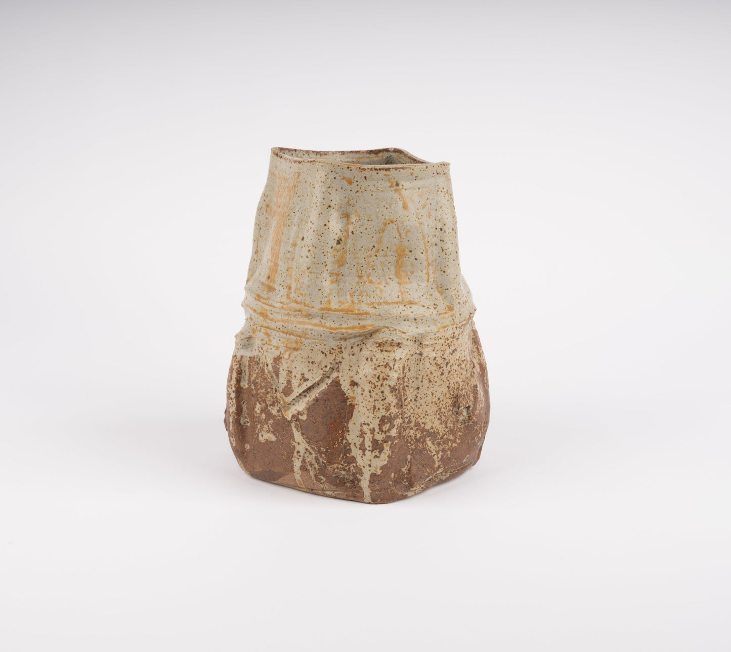 Wabi-Sabi inspired studio pottery vase with textured beige and brown glaze and irregular organic form on white background