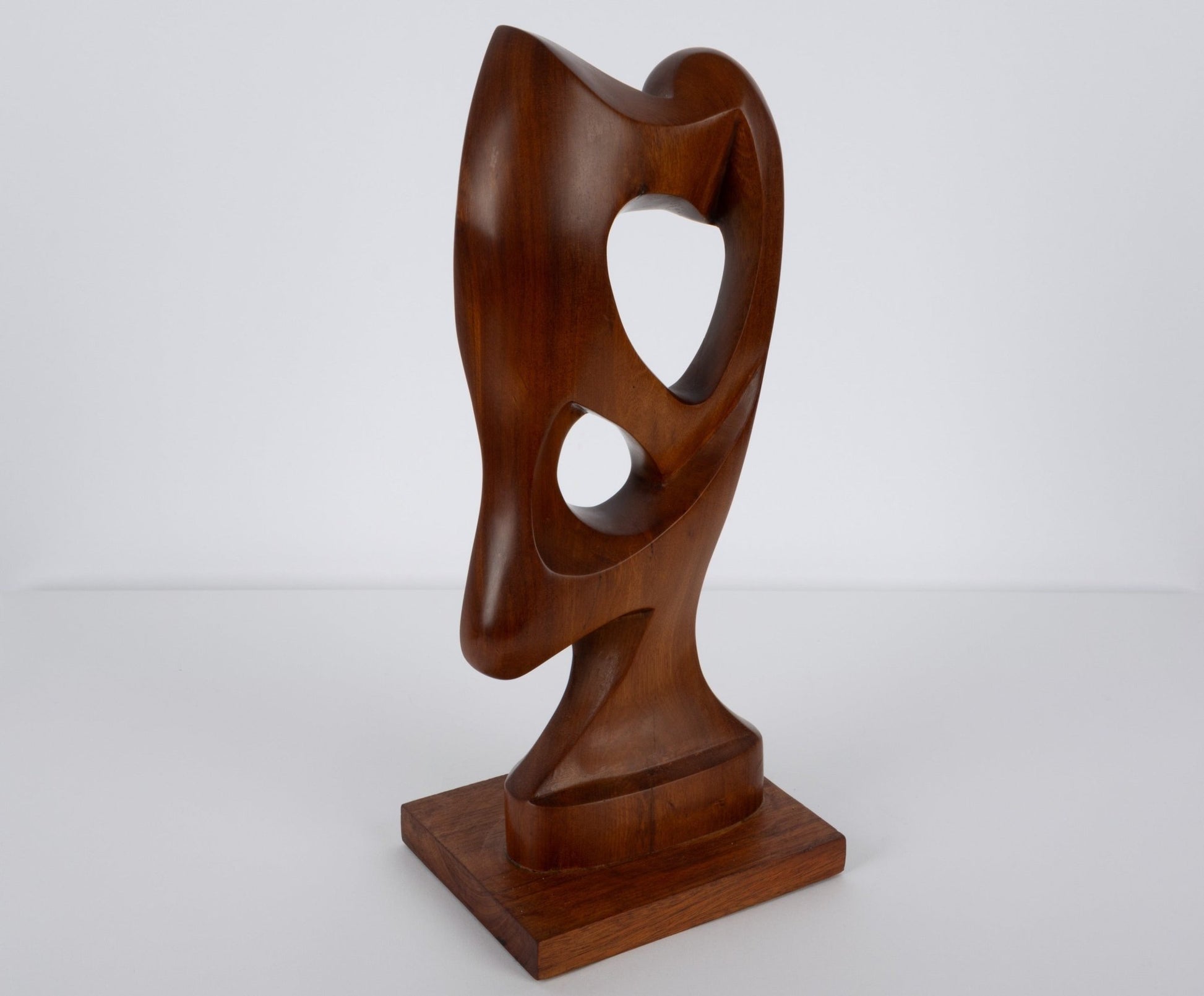 Abstract mid-century modern walnut sculpture with smooth curved shapes and organic cutouts on wooden base.