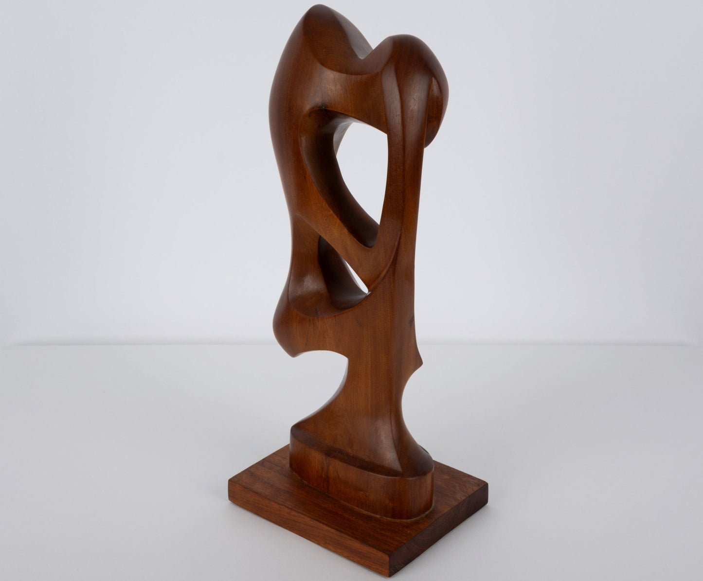 Abstract mid-century modern walnut sculpture with smooth organic curves on a rectangular wooden base.