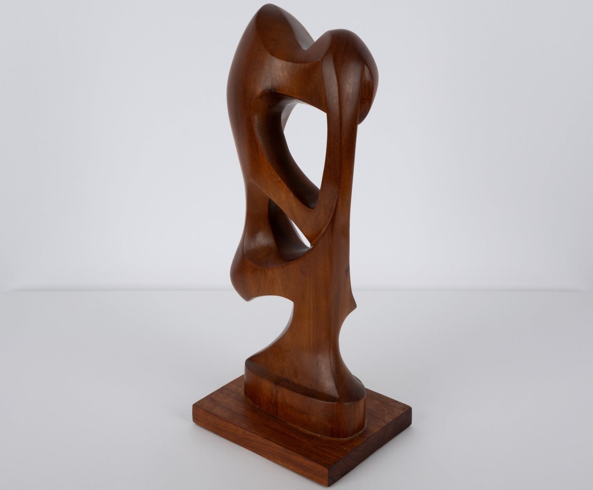 Abstract mid-century modern walnut sculpture with smooth organic curves on a rectangular wooden base.