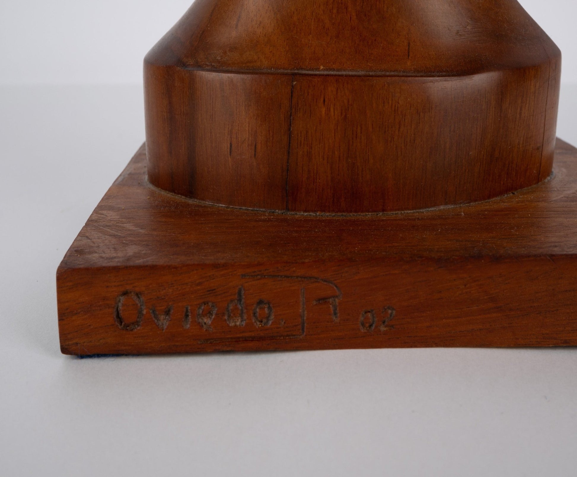 Close-up of solid walnut wooden sculpture base with carved signature and date on a plain white background