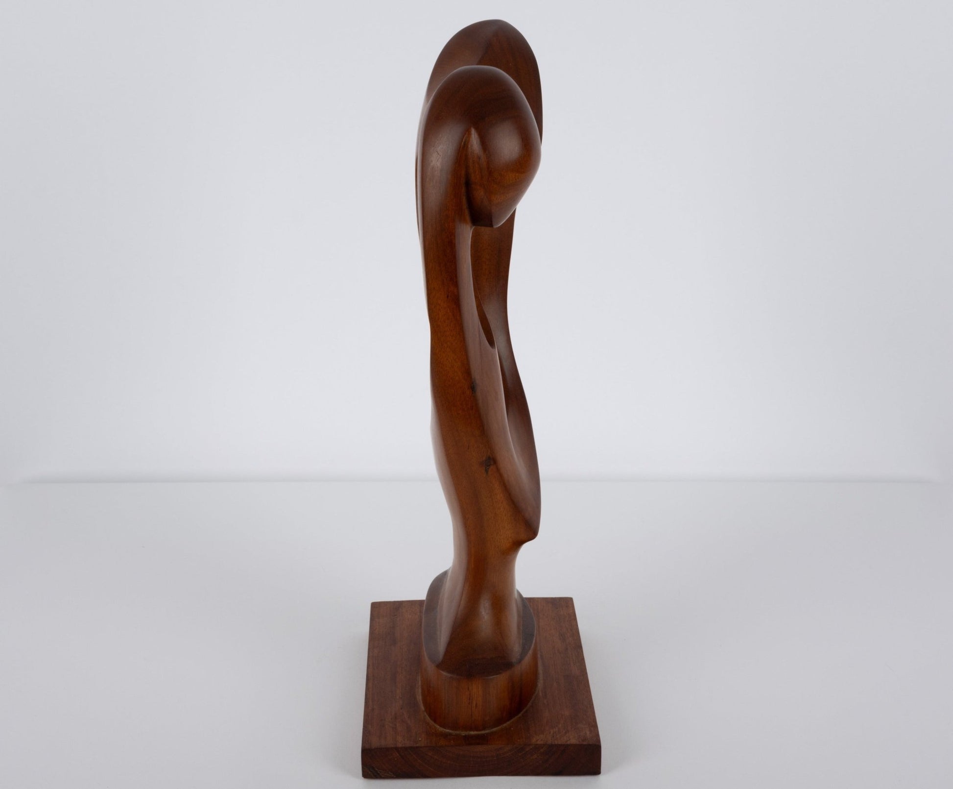 Abstract mid-century modern walnut sculpture with smooth curves, carved from a solid piece and mounted on a wooden base.