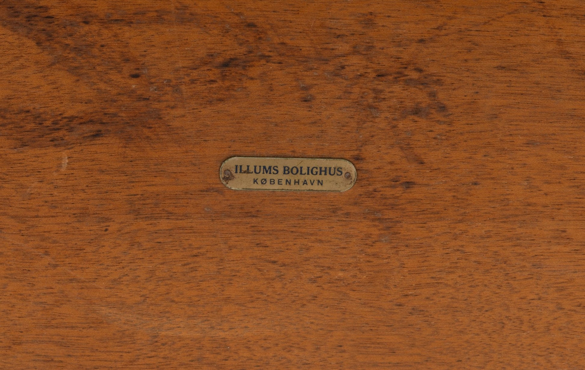 Close-up of brass Illums Bolighus label on rosewood surface of Yngvar Sandstrom coffee table for Seffle Mobelfabrik