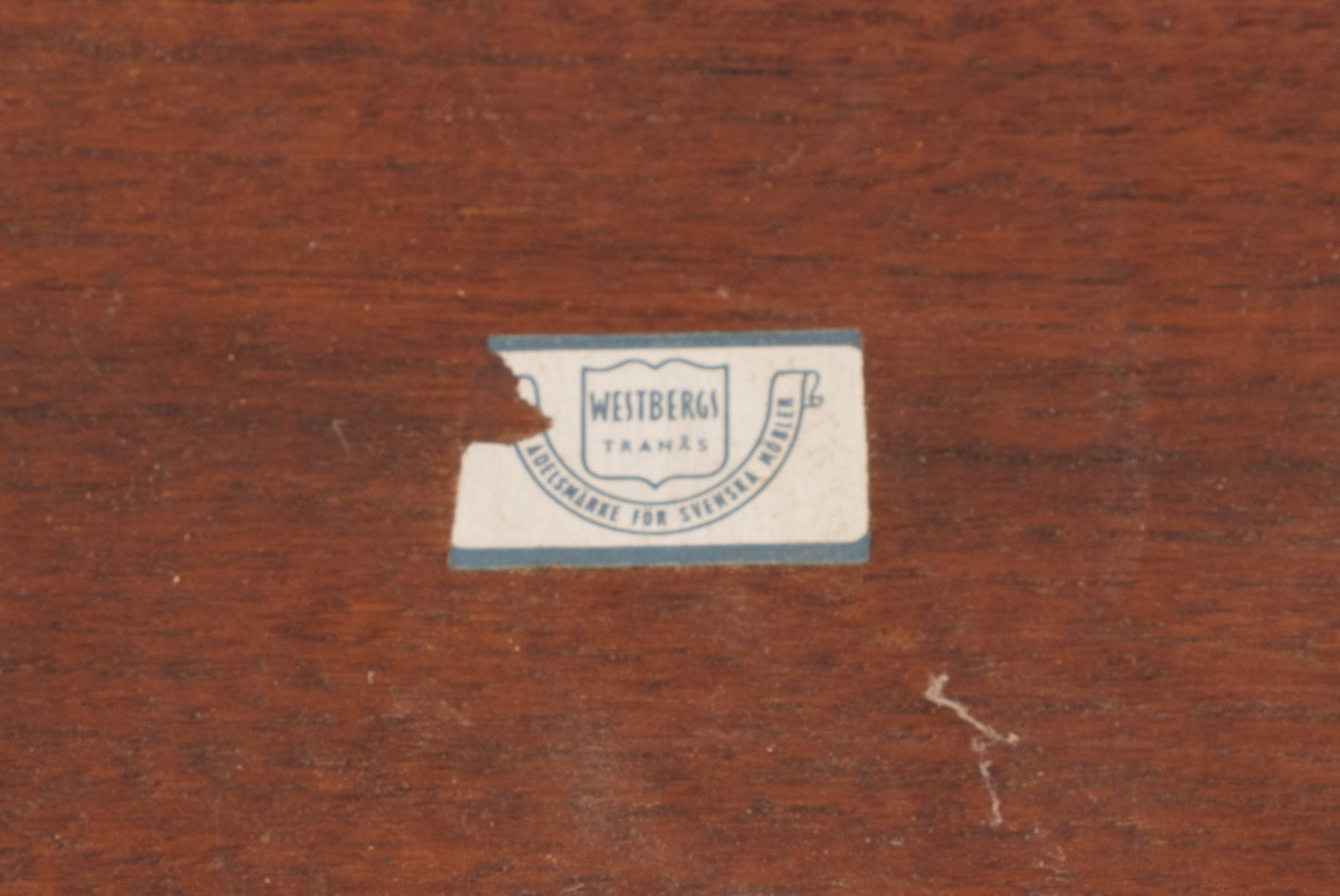 Close-up of a worn Westbergs Möbler label on mid-century modern teak coffee table surface.