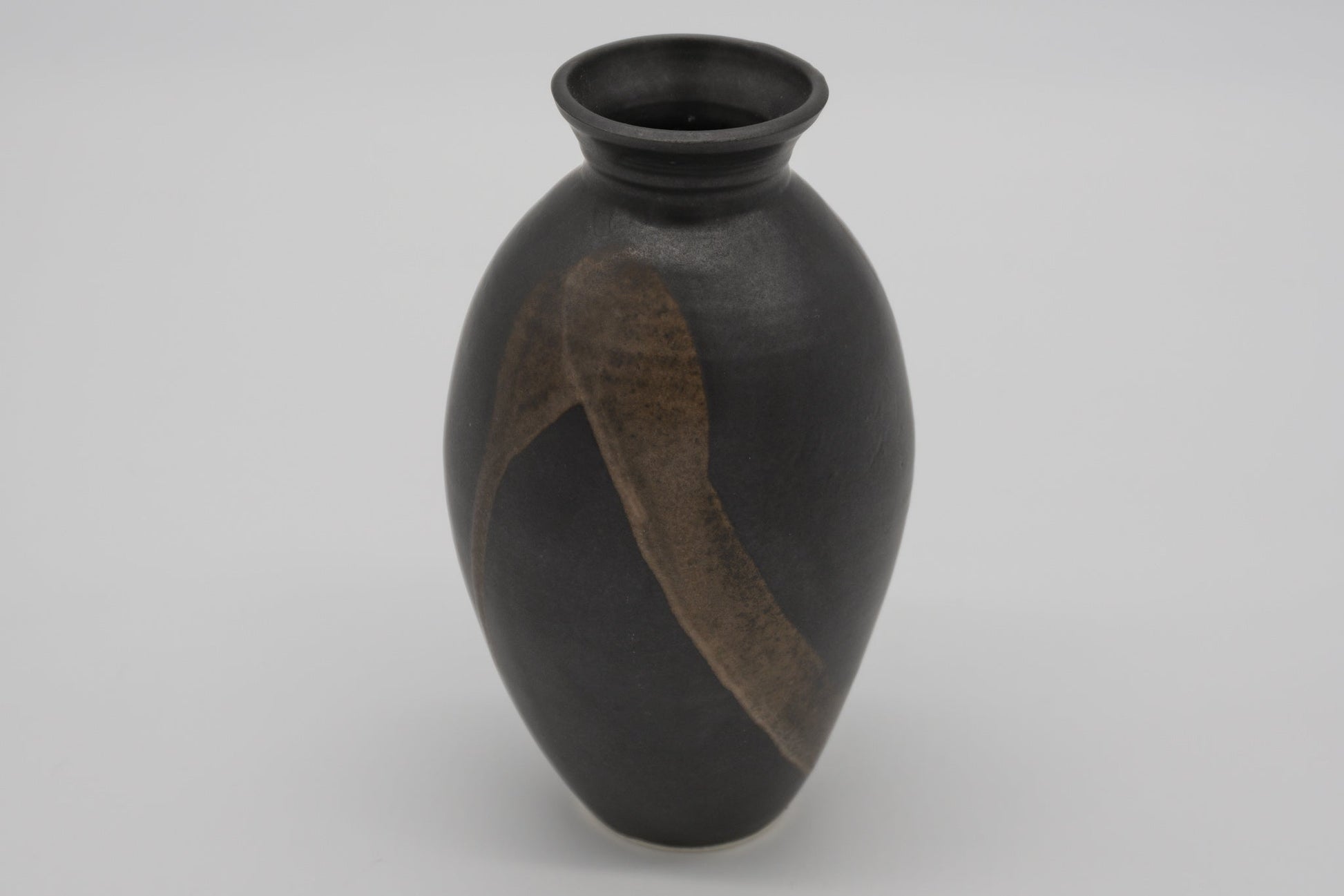 Studio pottery ceramic vase with dark glaze and semi-transparent brush marked strokes on the body, high choke neck.