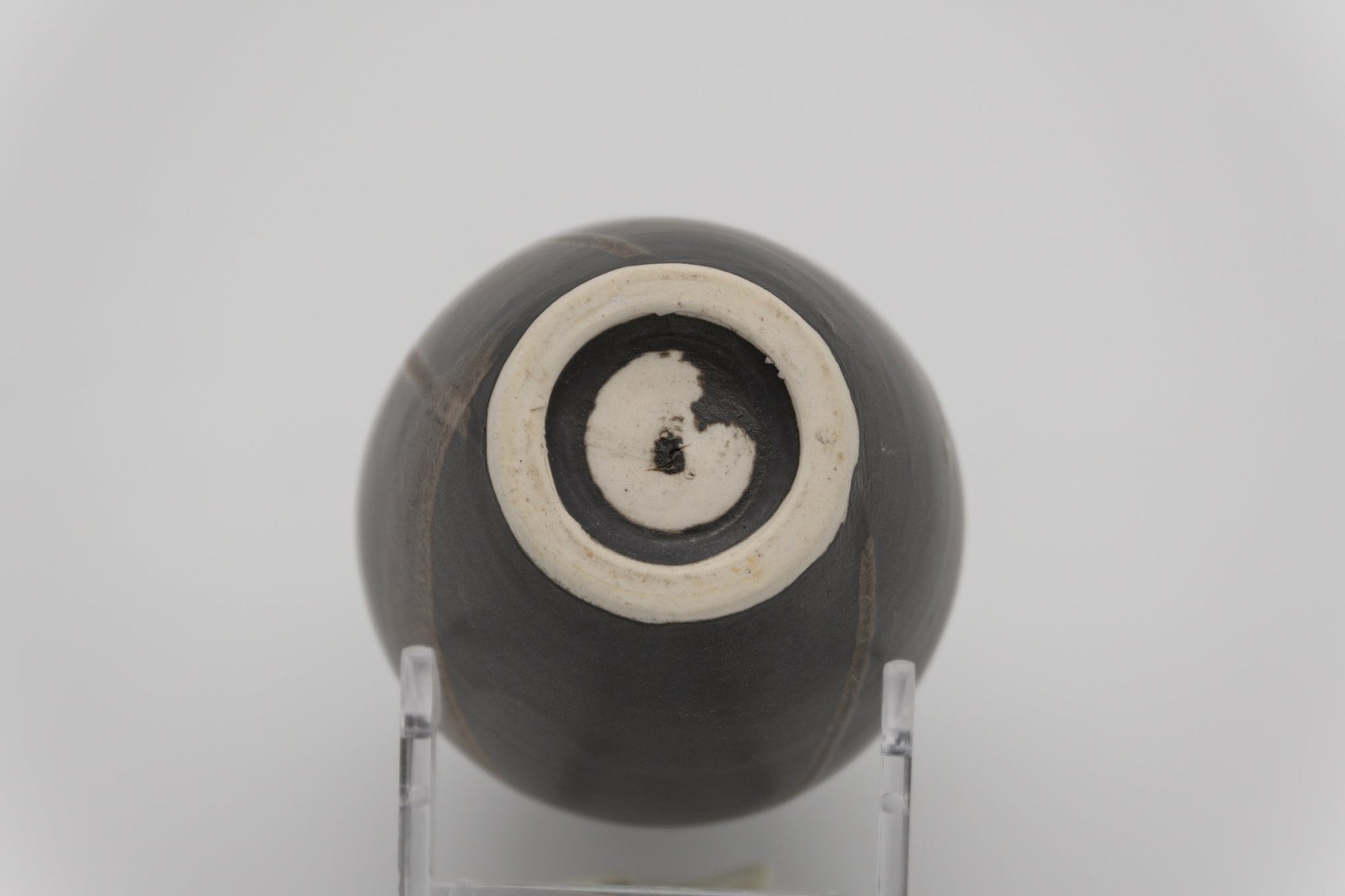 Bottom view of a dark glazed ceramic brush marked vase resting on a clear display stand