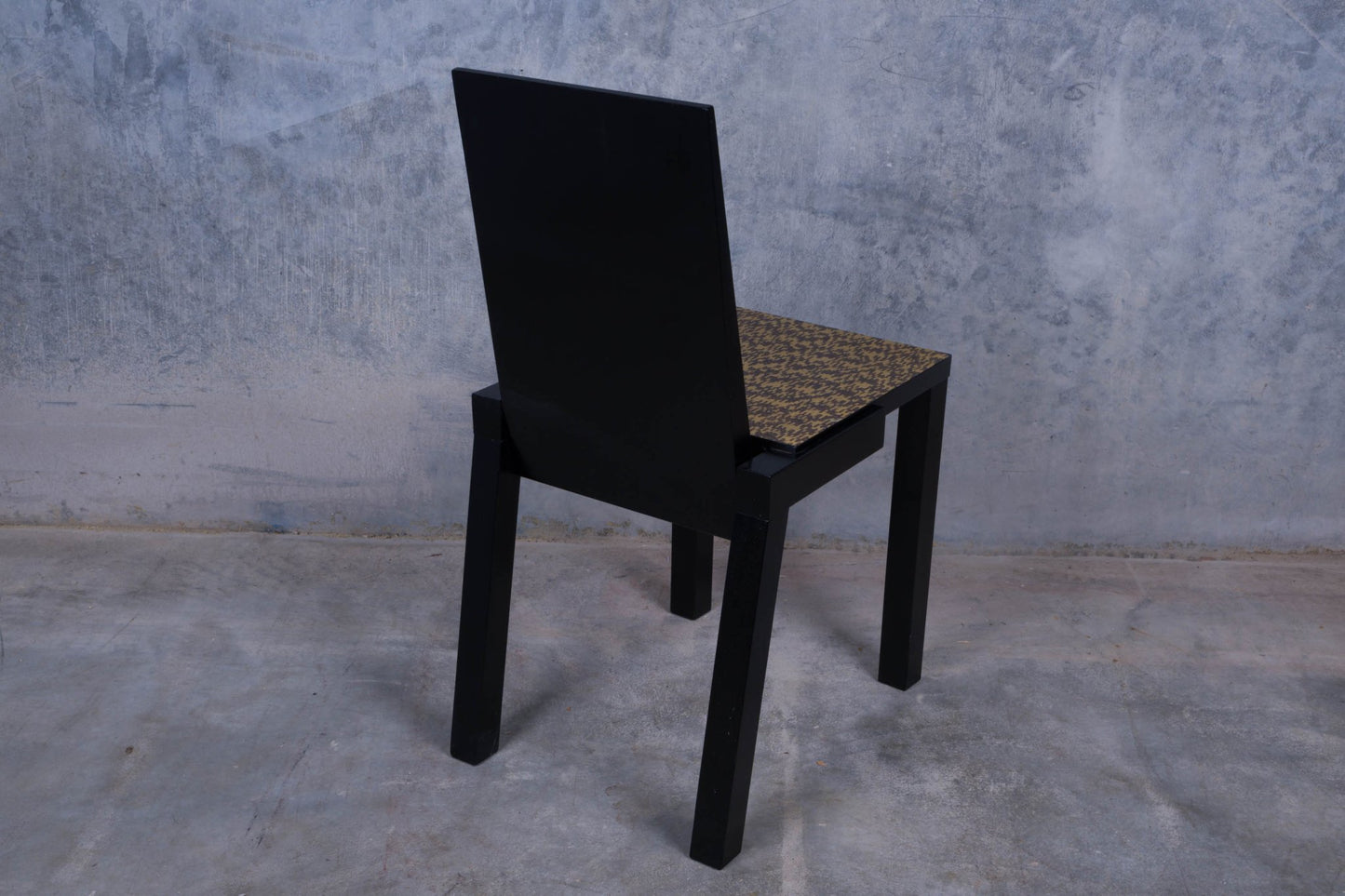 Constantin Boym black wooden chair with birdseye veneer seat and straight legs on a concrete floor background