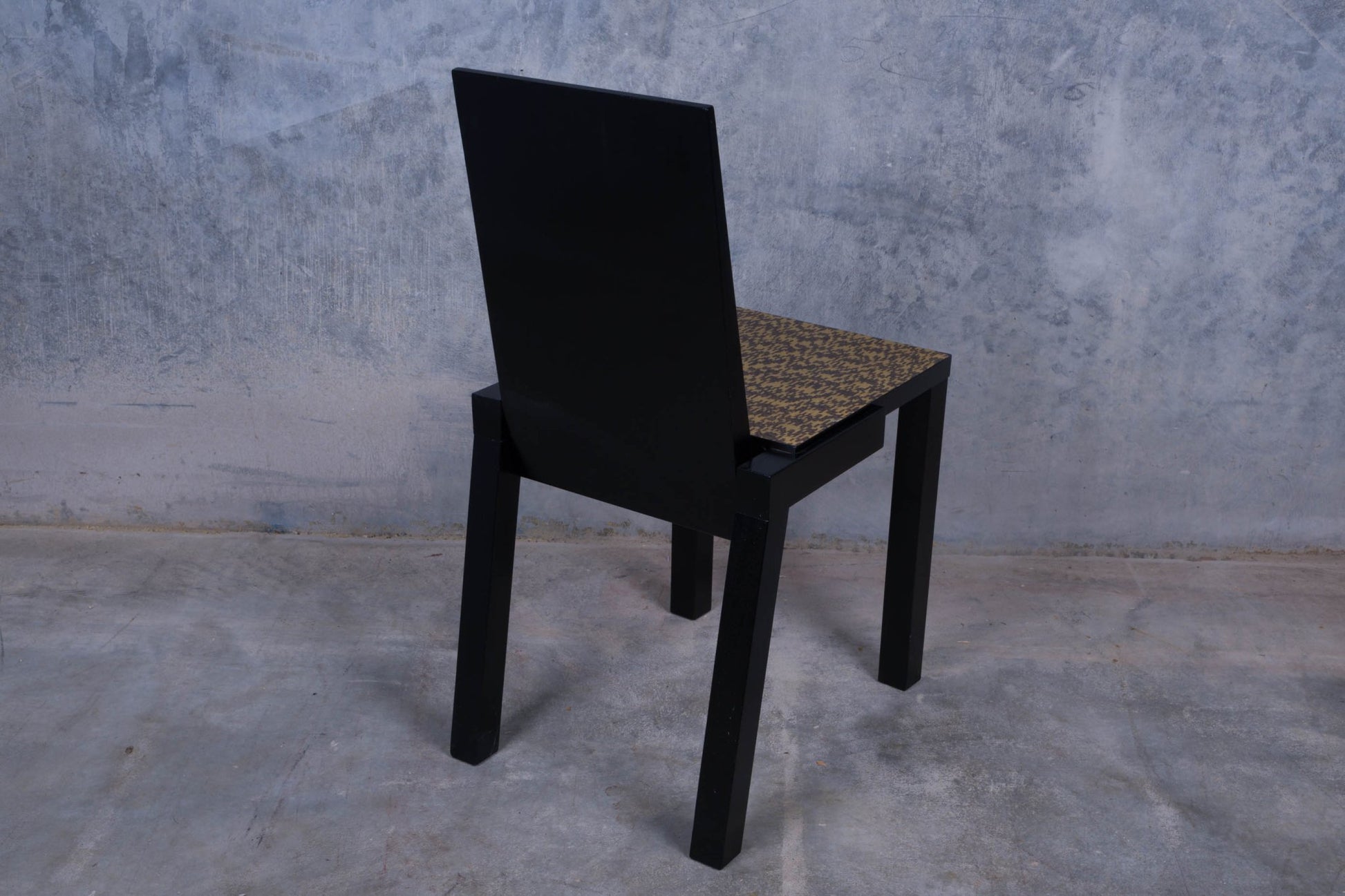 Constantin Boym black wooden chair with birdseye veneer seat and straight legs on a concrete floor background