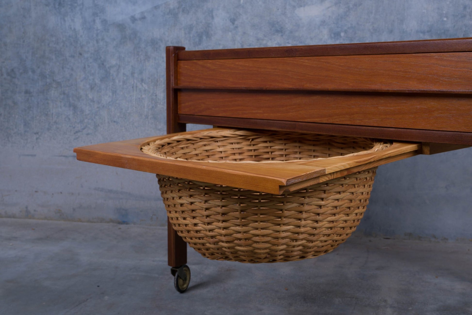 Close-up of mid-century Danish teak sewing side table with pull-out caned circular basket and caster wheels.