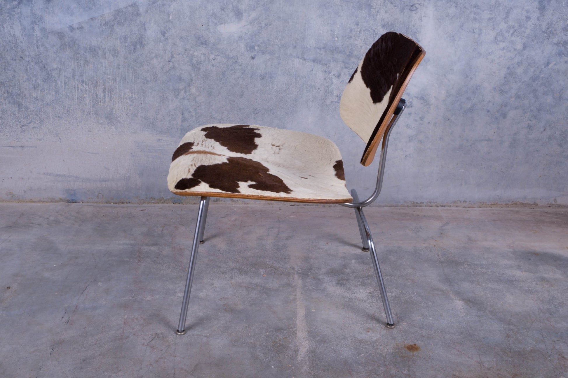 Side view of Charles Eames Cowhide Lounge Chair with molded plywood frame and chrome legs on concrete floor