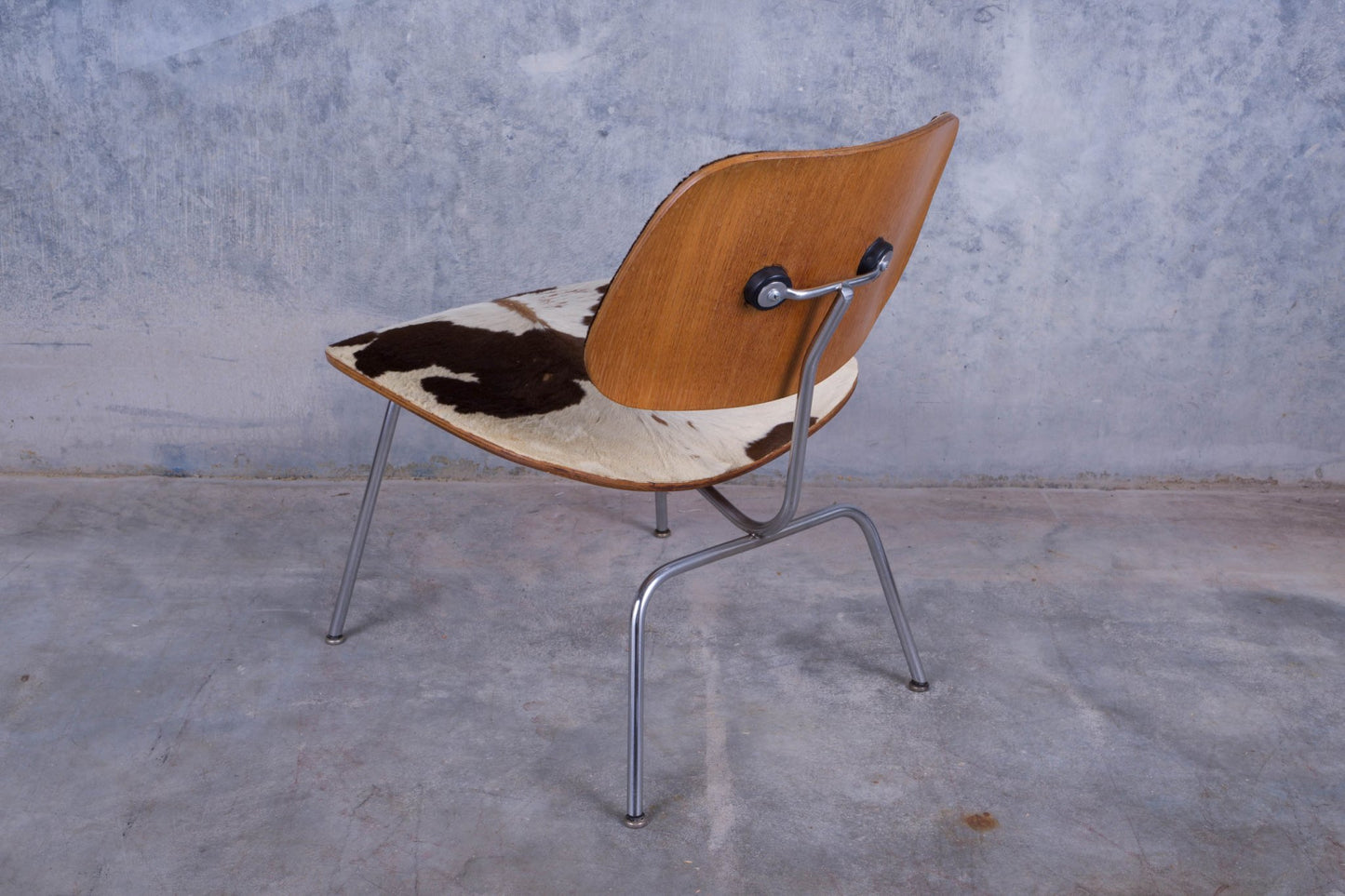 Rear view of Charles Eames lounge chair with cowhide upholstery and molded plywood backrest on metal legs