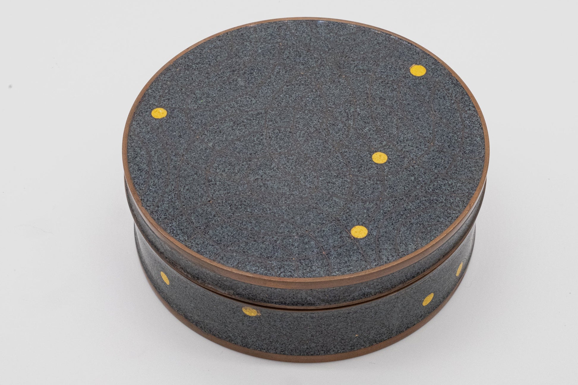 Round Fabienne Jouvin copper canister with black speckled background, bronze spherical pattern, and yellow dot accents