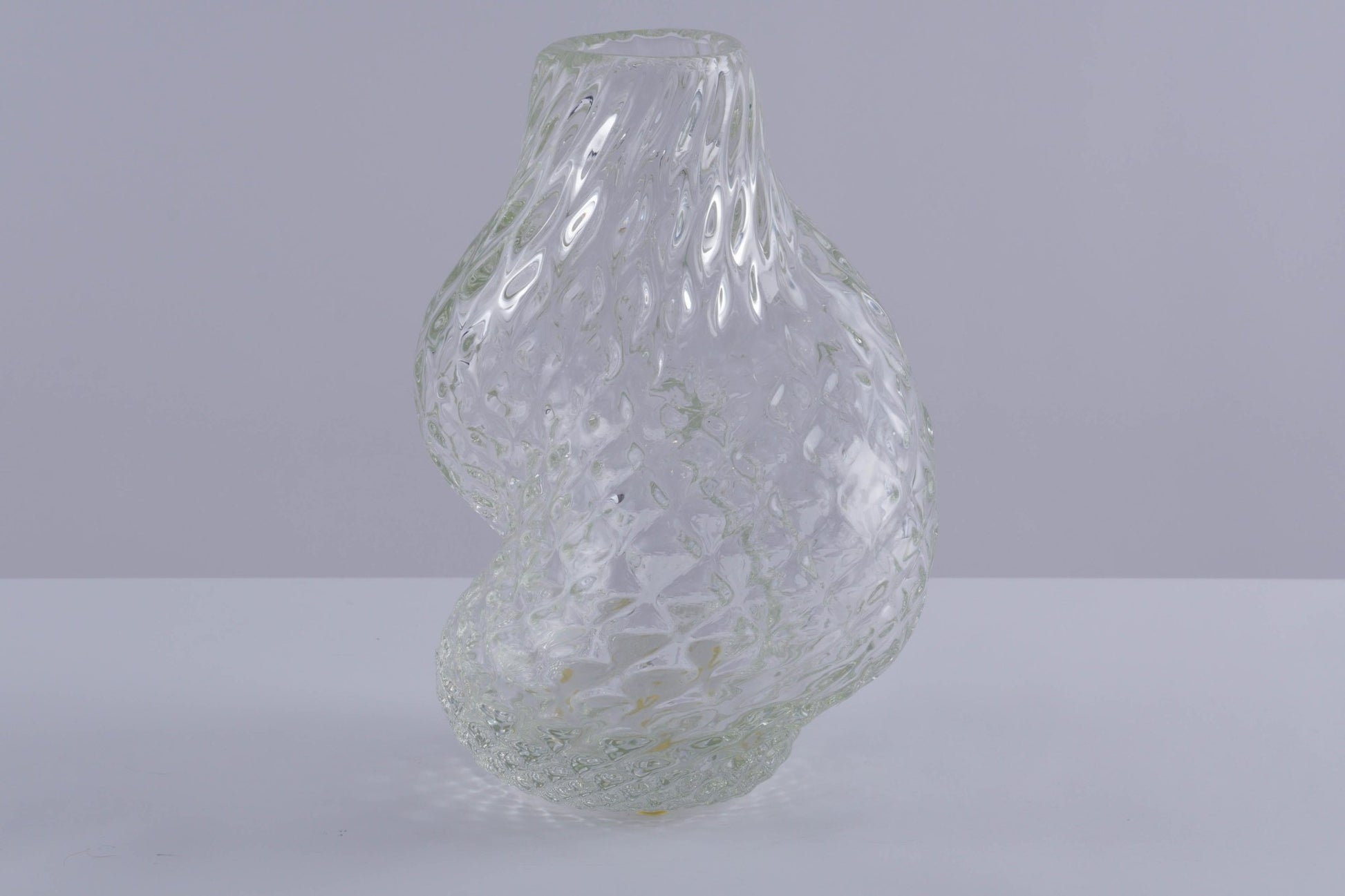 Asymmetrical clear glass vessel by Flavio Poli with spiral textured surface on neutral background.