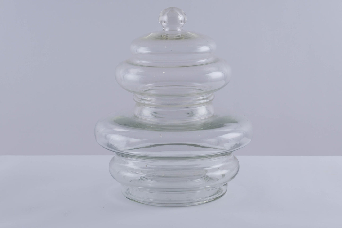 Large clear glass jar vessel with rounded lid and smooth tube-shaped body tapering outward from base.
